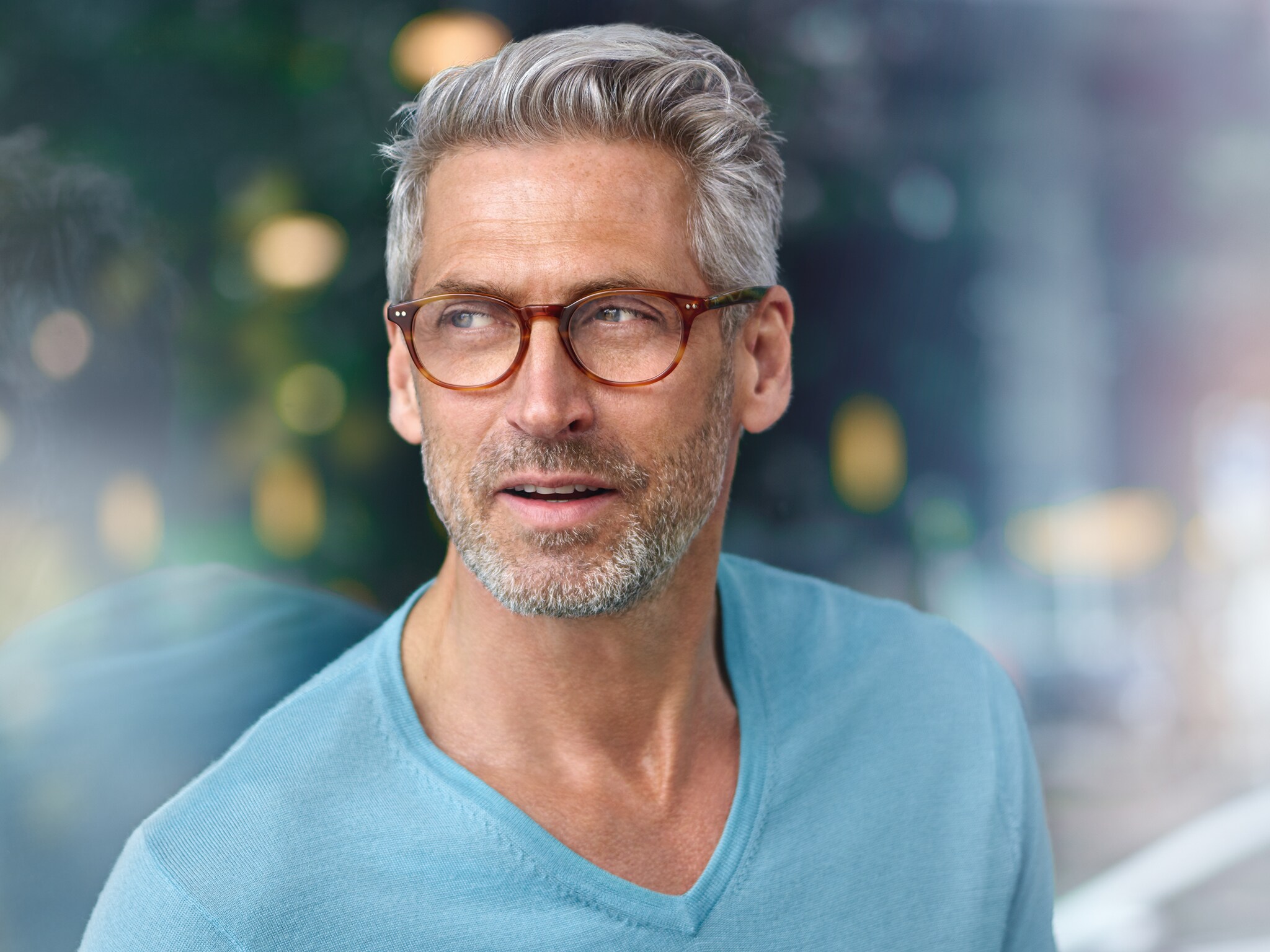 Mężczyzna w okularach na tle szklanej elewacji budynku.