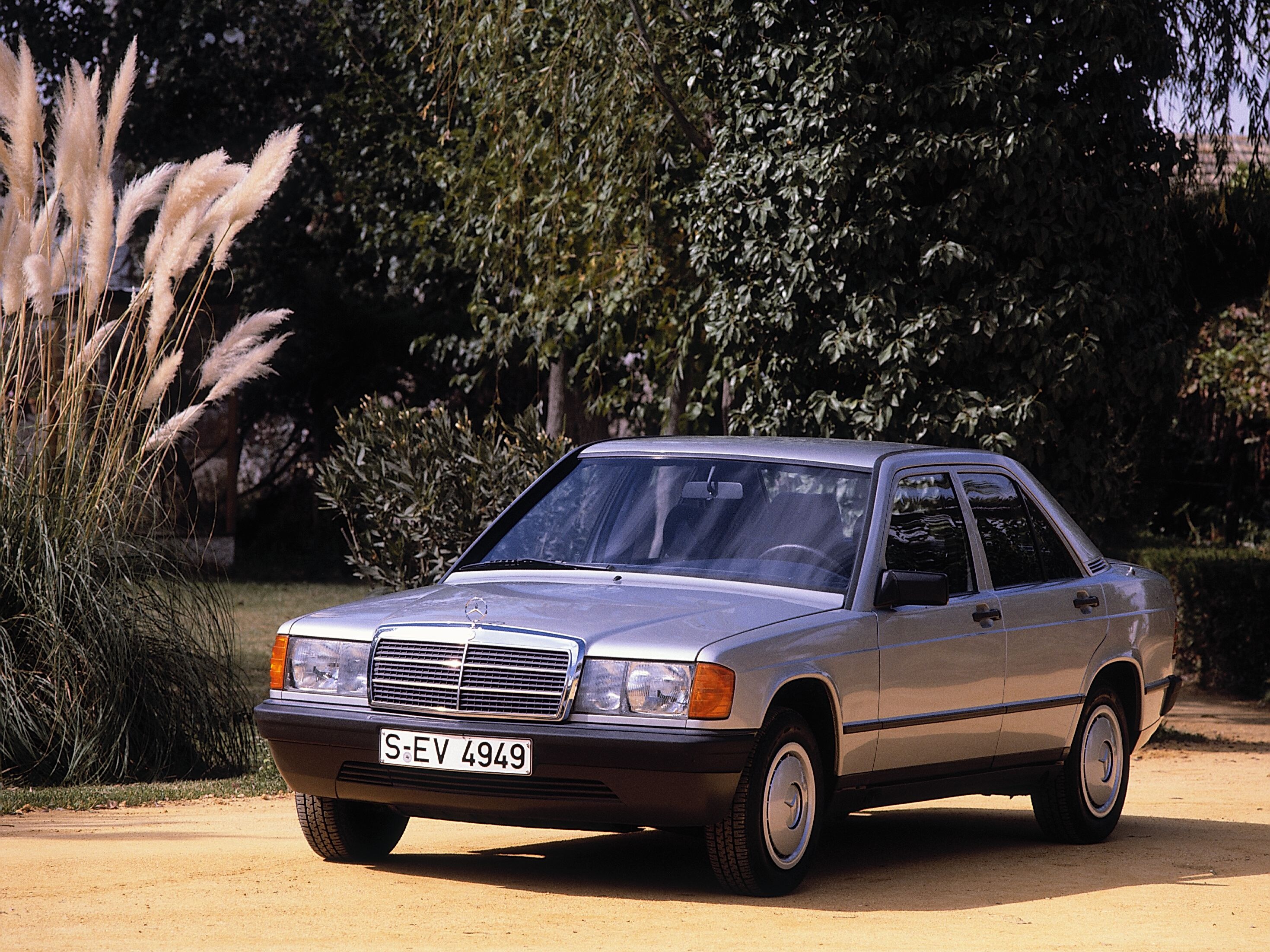 Srebrny Mercedes-Benz 190 E  stoi zaparkowany na tle zieleni.