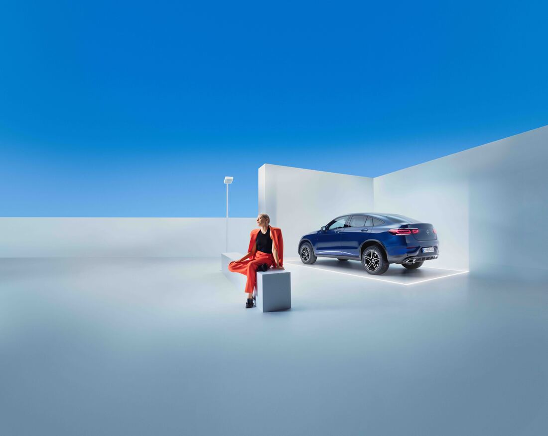 Pakiety serwisowe Mercedes-Benz. Kobieta siedzi na ławce obok ciemnoniebieskiego Mercedesa GLC.