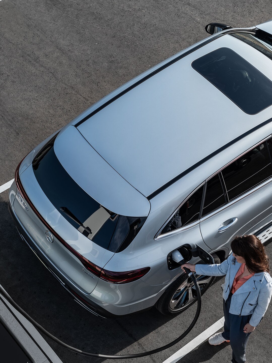 Kobieta podłącza swojego Mercedesa do stacji ładowania.