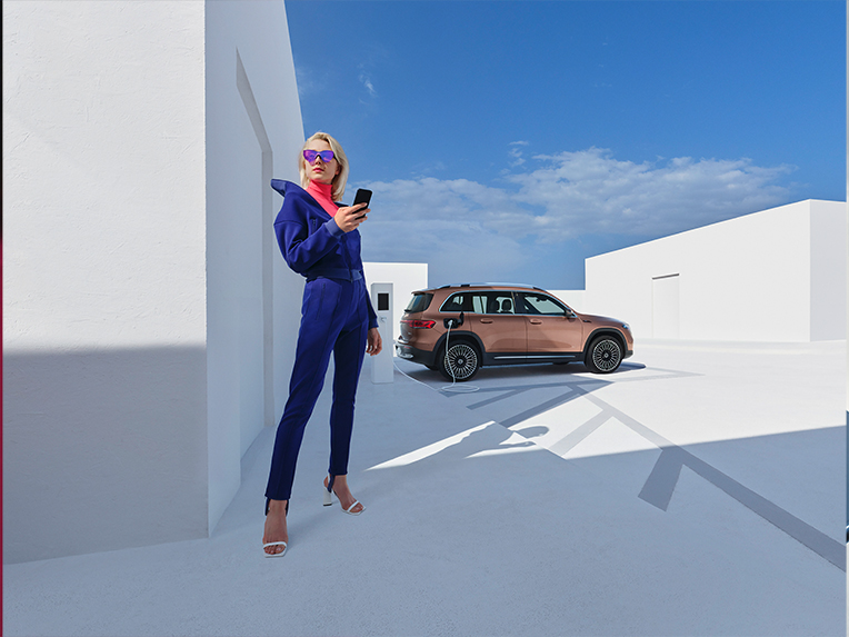 Aplikacje Mercedes-Benz | Cyfrowe Dodatki | Mercedes-Benz Kobieta trzyma w ręku smartfona na tle Mercedesa EQB.