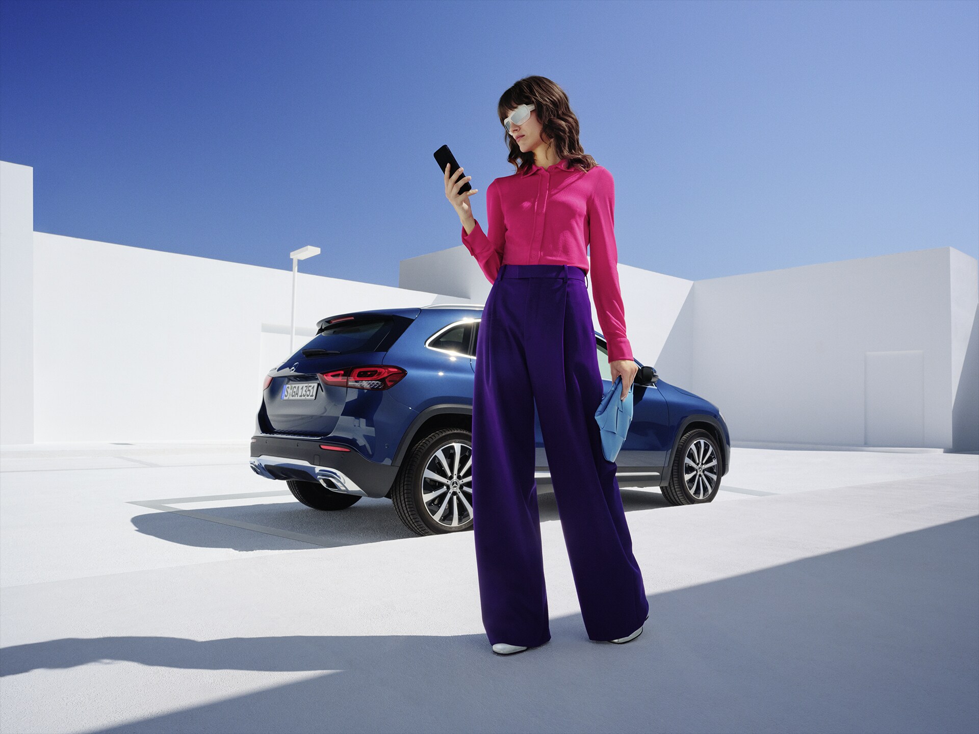 Kobieta stoi przed samochodem Mercedes-Benz GLA i patrzy na swój telefon.