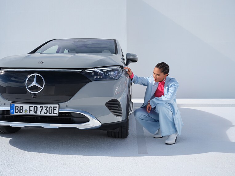 Kobieta kuca przy szarym Mercedesie EQE SUV.