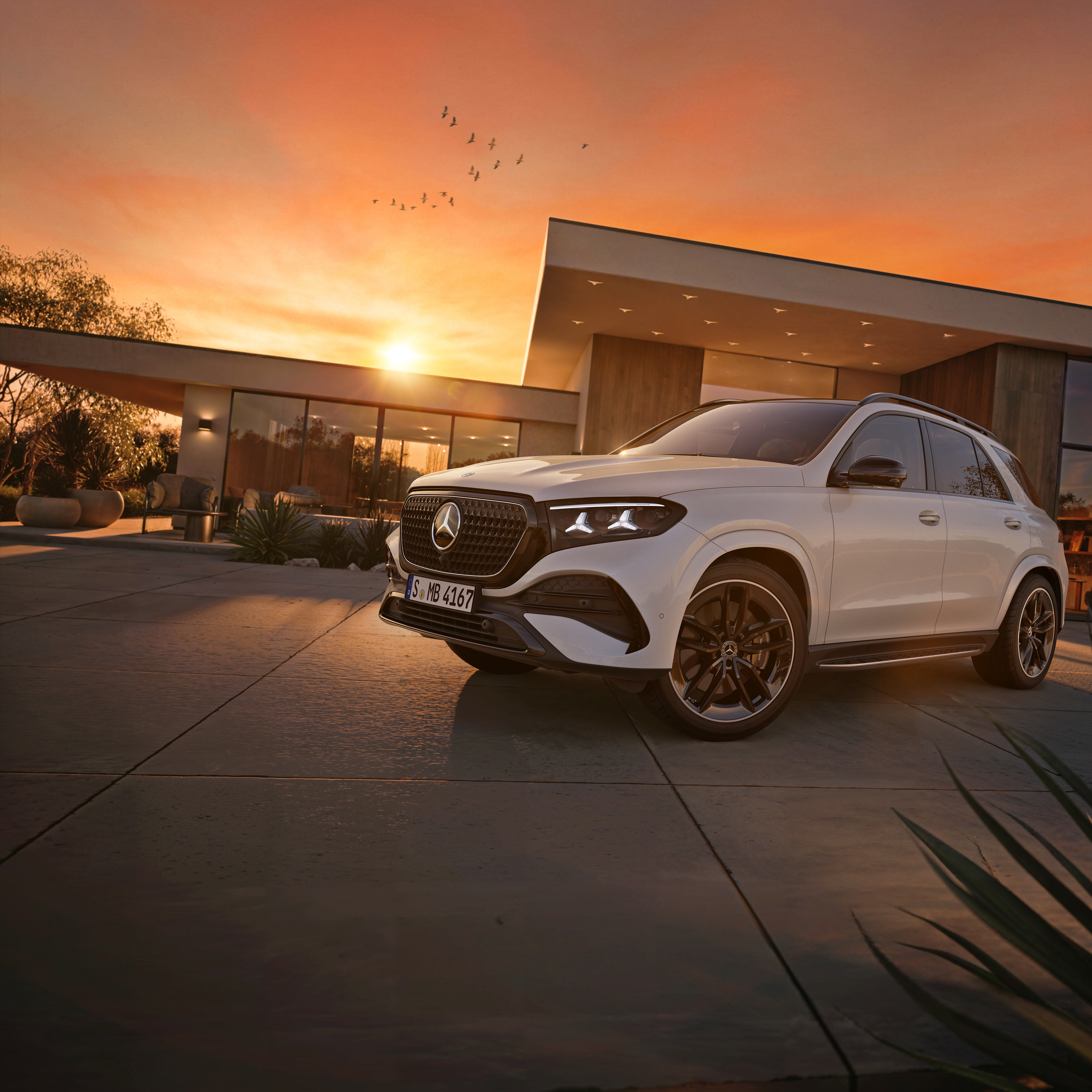 Powitaj jesień z Mercedes-Benz Biały Mercedes-Benz GLE SUV zaparkowany przed domem na tle zachodzącego słońca.
