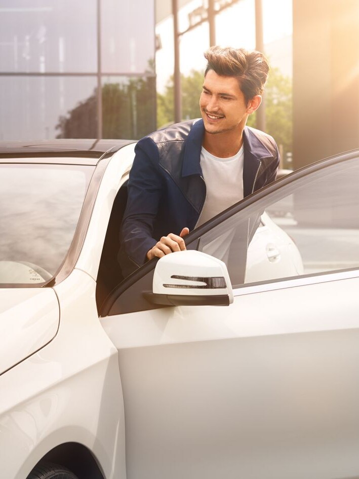 Mężczyzna wsiada do białego Mercedesa.