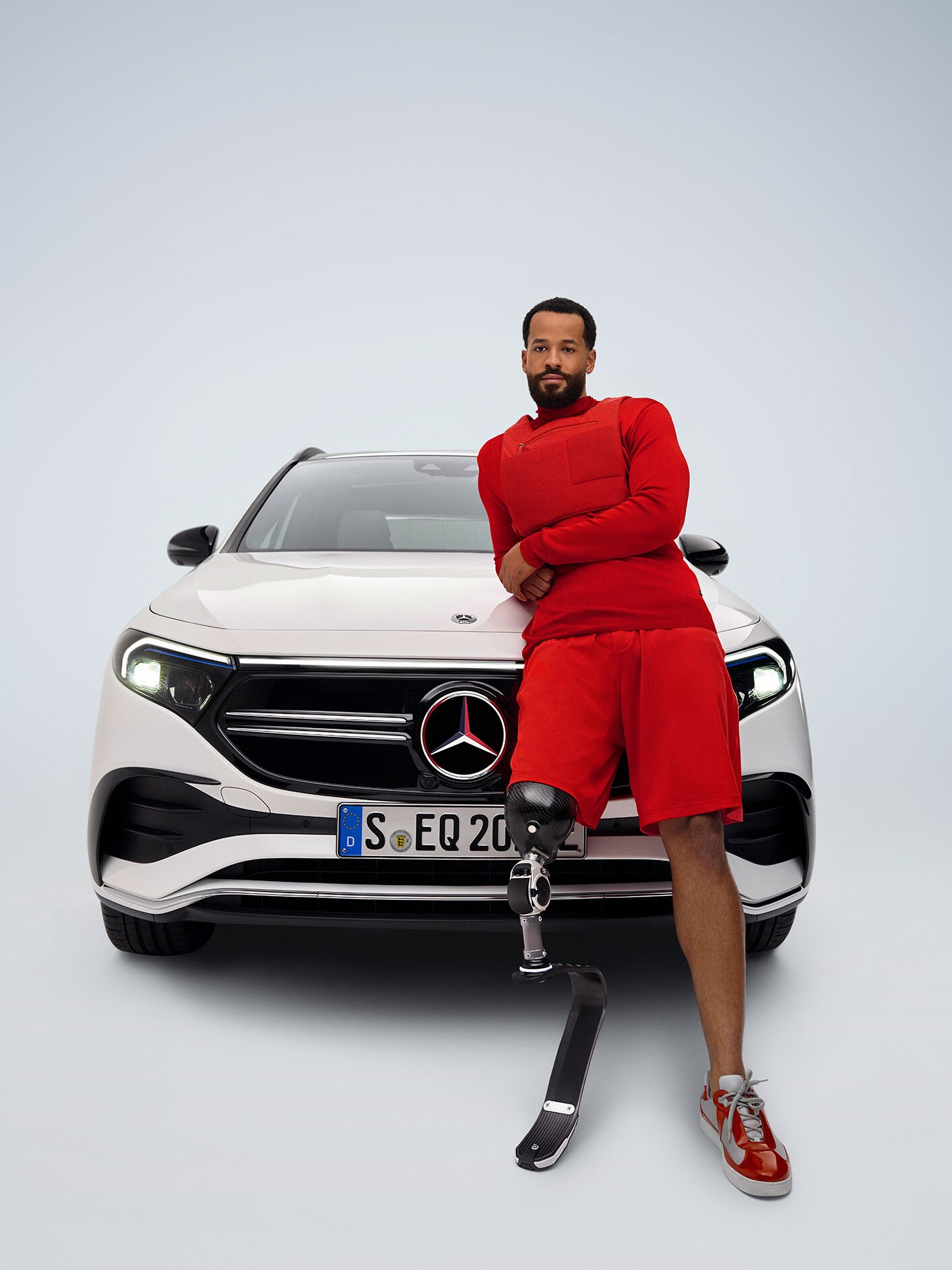 Mężczyzna z protezą nogi opiera się o Mercedesa EQA.