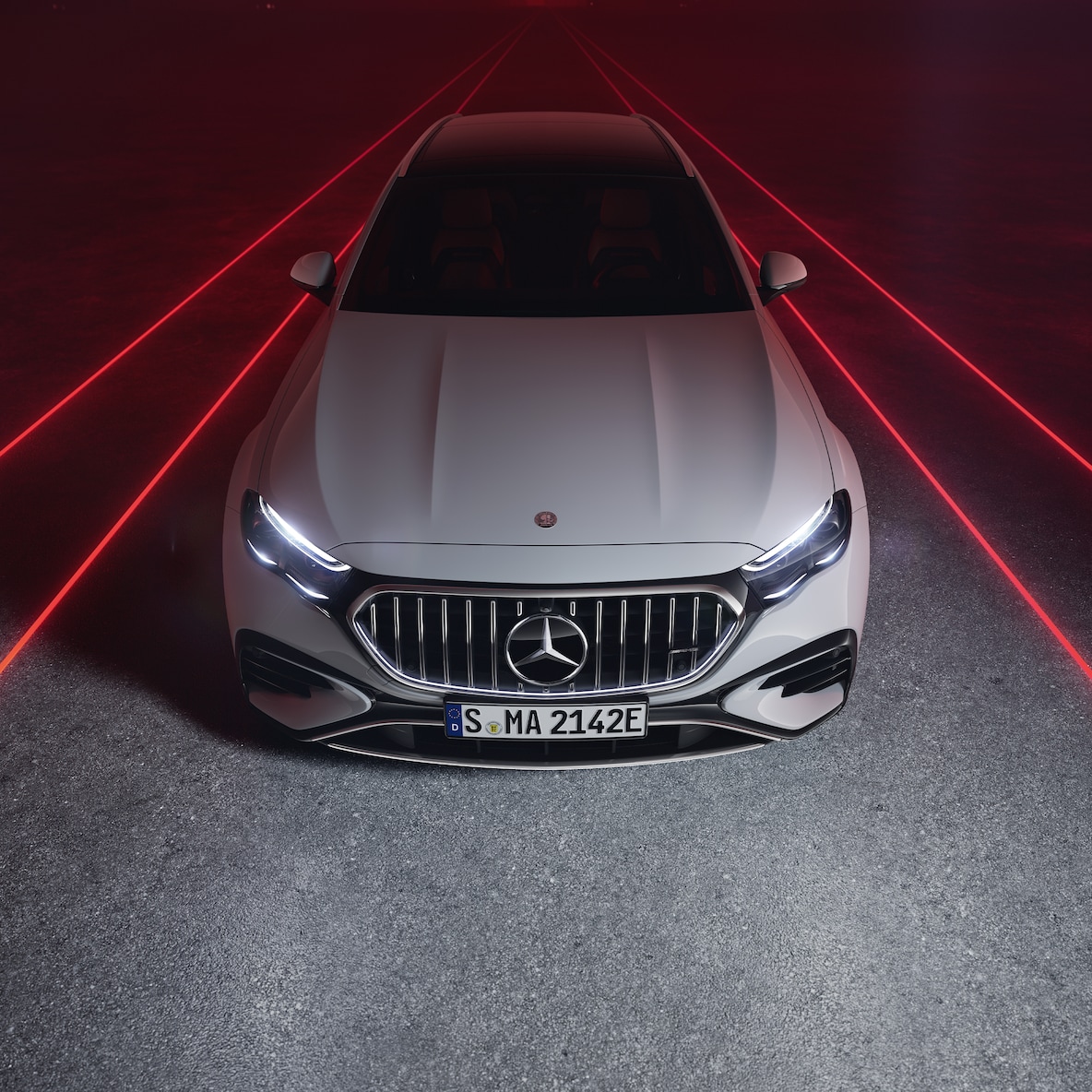 Mercedes-AMG E 53 HYBRID 4MATIC+ widoczny od przodu na czerwonym tle, widok z góry.