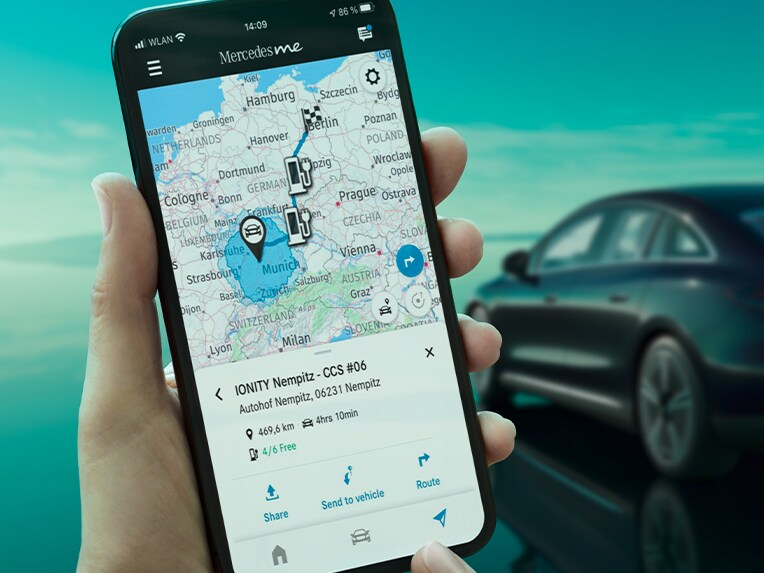 Aplikacja ECO Coach na smartfonie, a w tle limuzyna EQE ładujący się przy wallboxie.