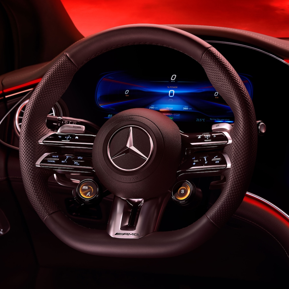 Widok kierownicy AMG Performance z fotela kierowcy na czerwonym tle.