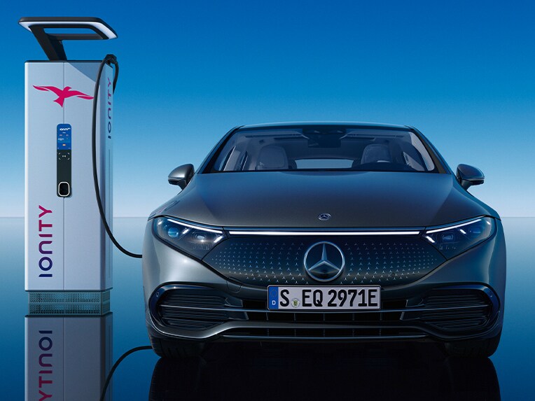 Widok z przodu limuzyny EQS od Mercedes-Benz ładującej się na publicznej stacji ładowania.