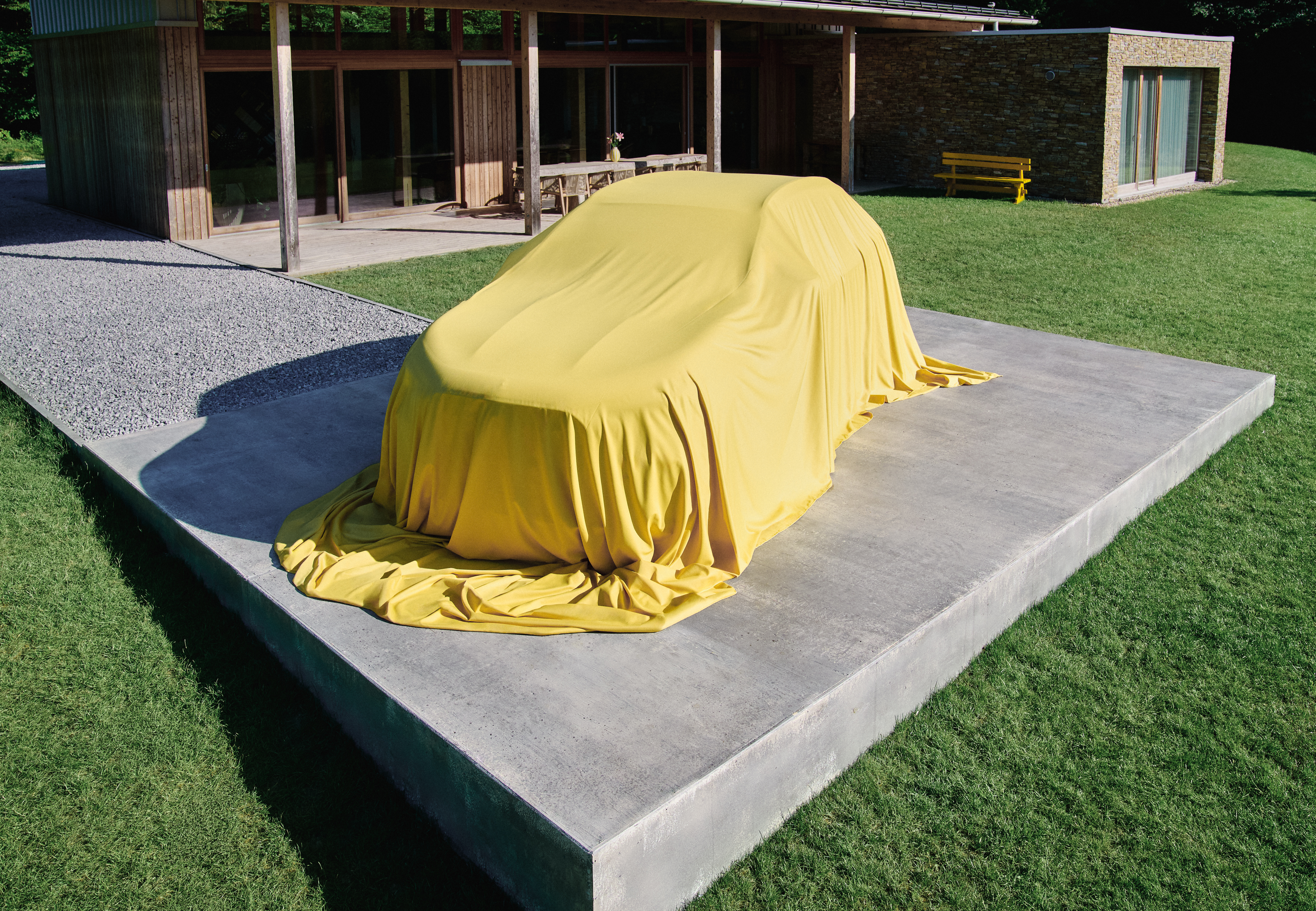 Zasłonięty całkowicie nowy Mercedes-Benz GLA jest pokazany z boku w trzech czwartych na parkingu na tle domu mieszkalnego.
