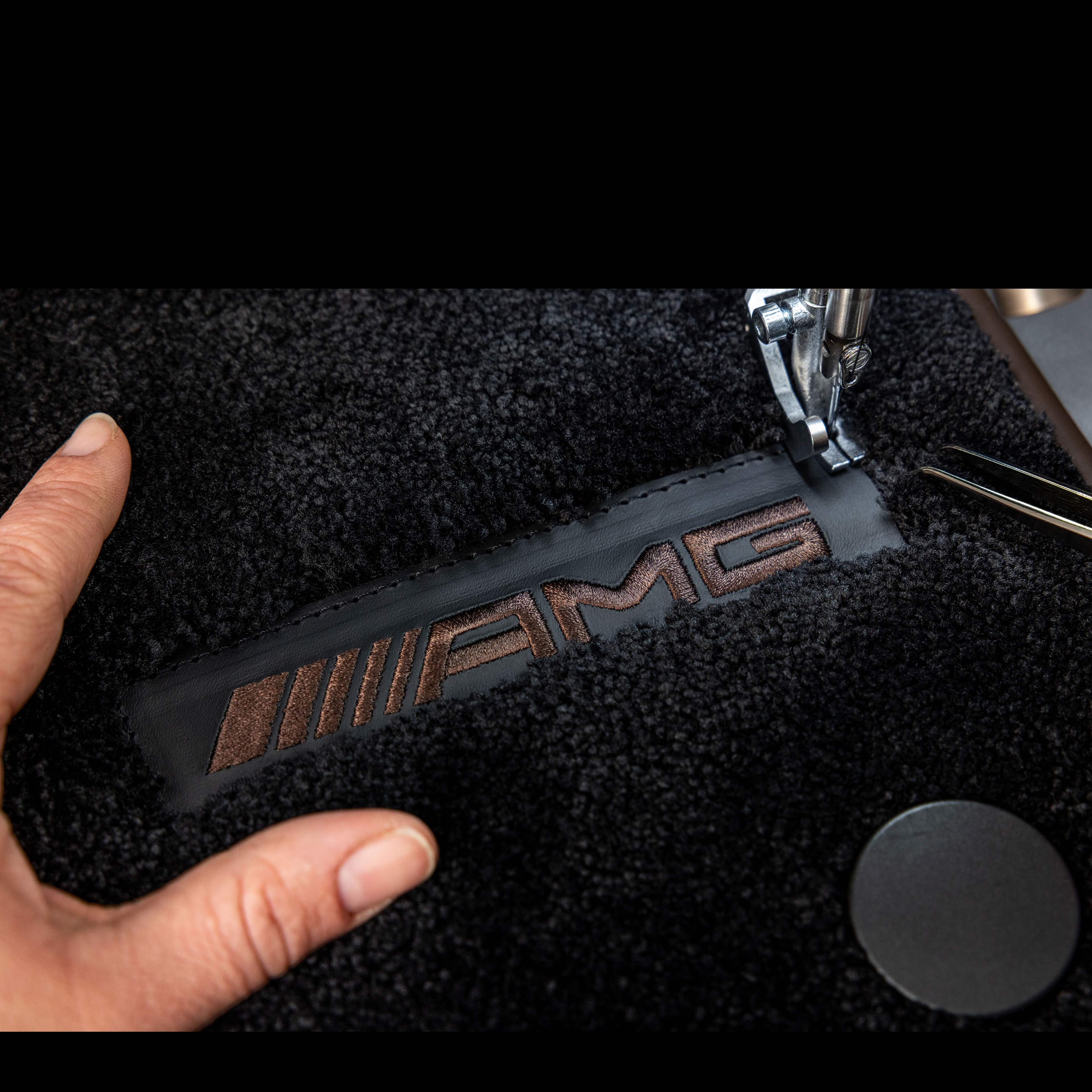 MANUFAKTUR | Mercedes-AMG Emblemat MANUFAKTUR na ciemnej powierzchni w samochodzie Mercedes-AMG.