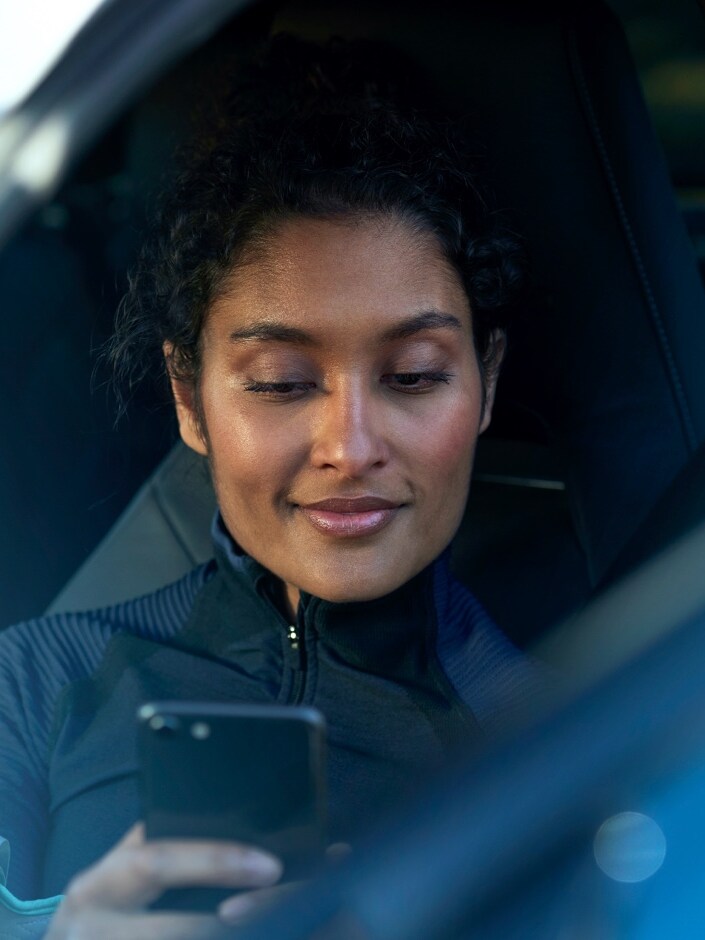 Kobieta siedząca na miejscu pasażera korzysta ze smartfona.