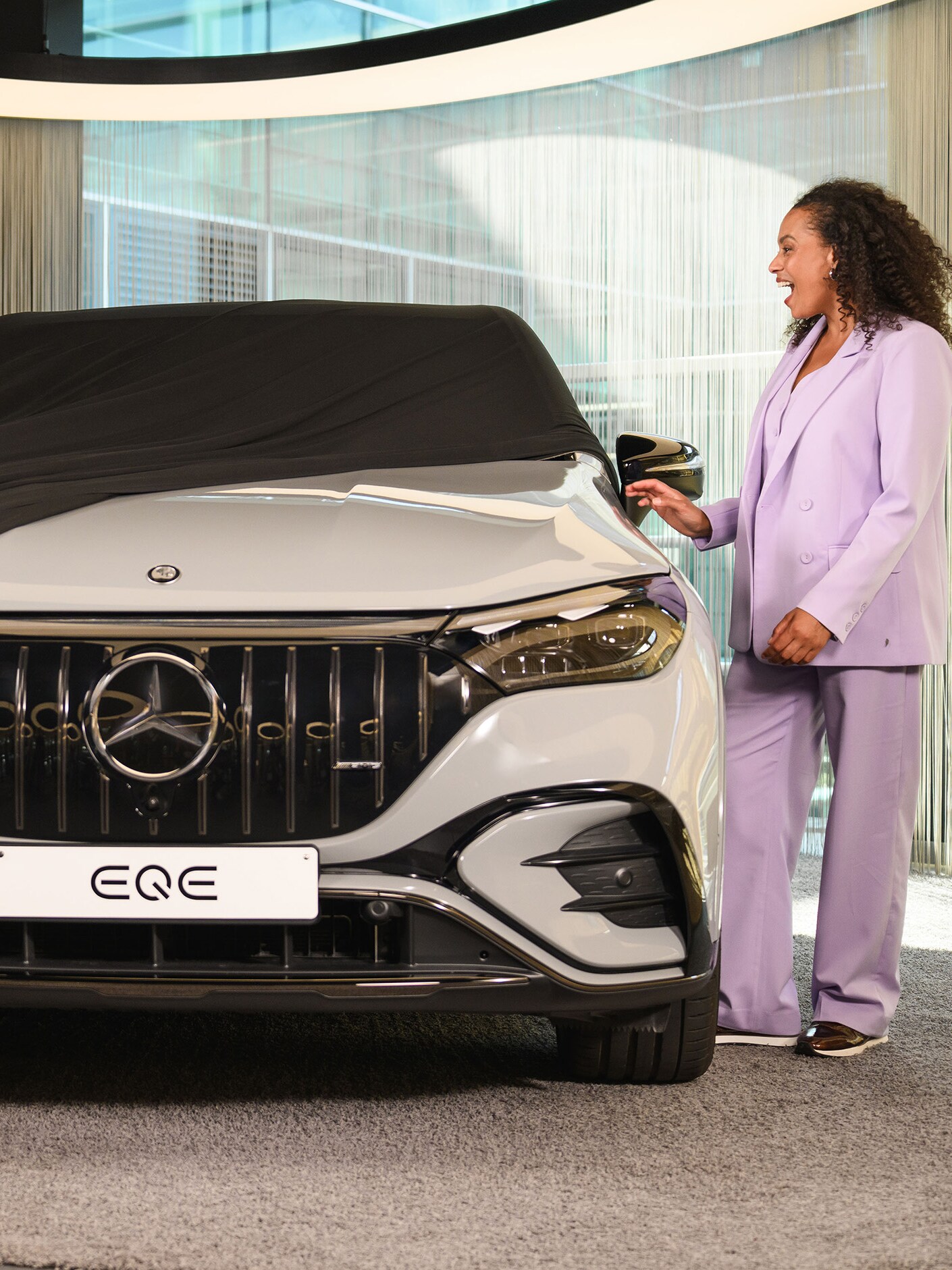 Kobieta zdejmuje pokrywę z nowego Mercedesa EQE SUV w salonie samochodowym.