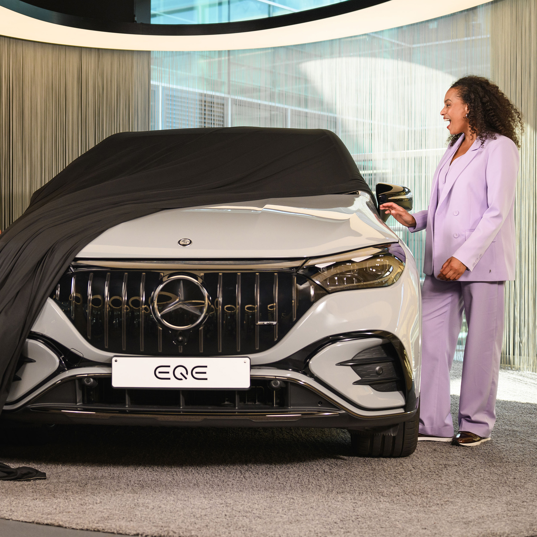 Oferta na nowy pojazd | Mercedes-Benz Kobieta zdejmuje pokrywę z nowego Mercedesa EQE SUV w salonie samochodowym.