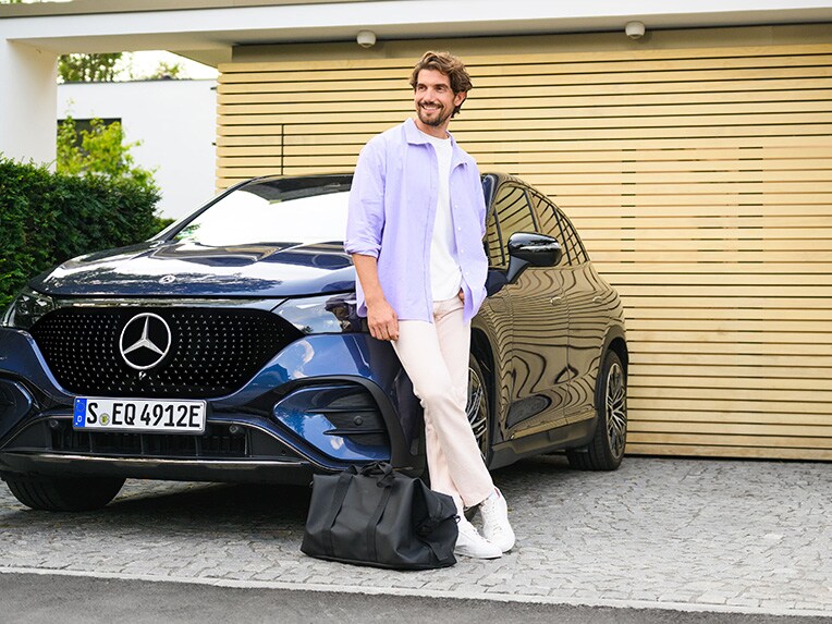 Mężczyzna opiera się o Mercedesa EQE SUV i patrzy w lewą stronę.