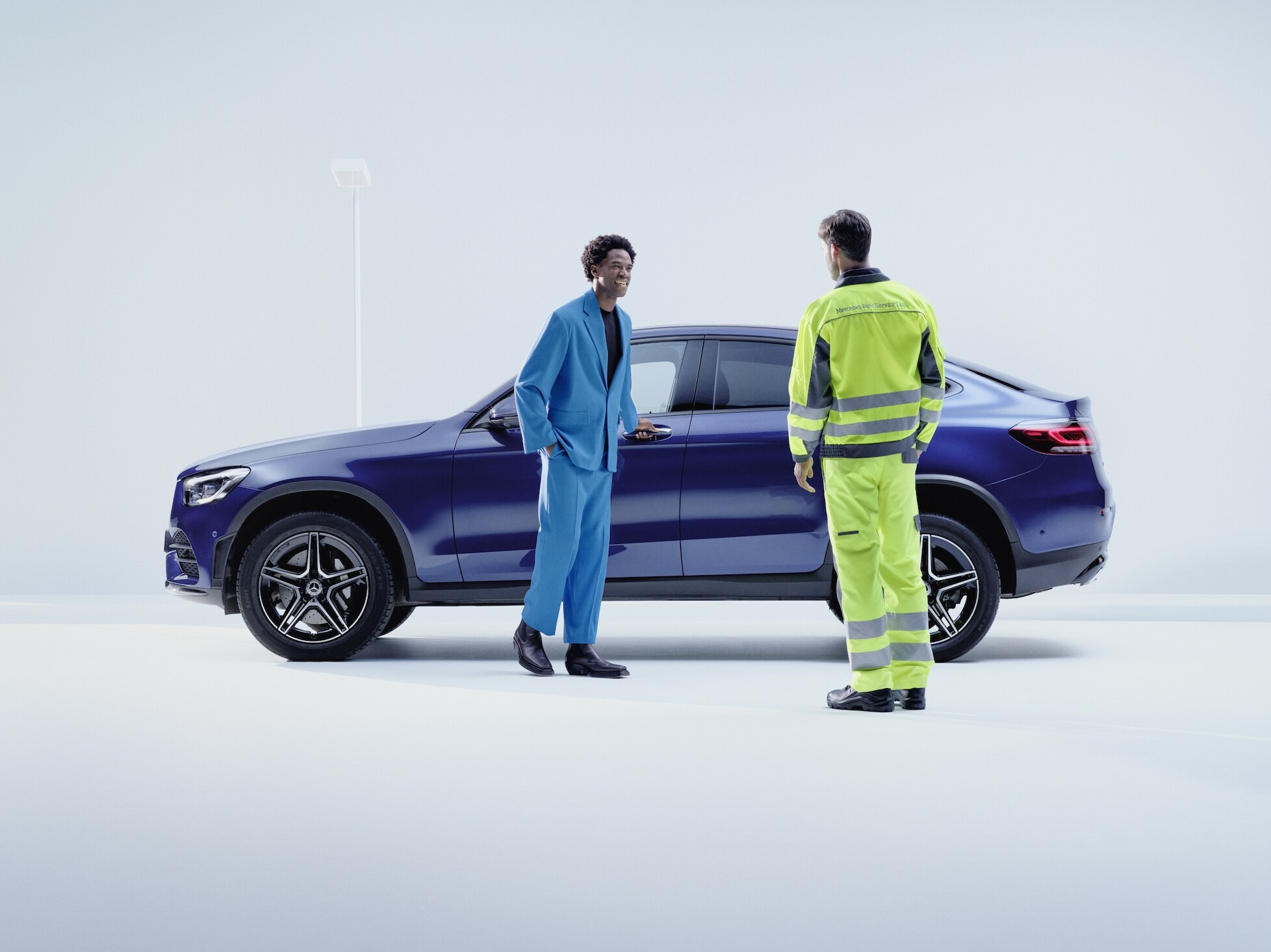 Pracownik serwisu Mercedes-Benz rozmawia z klientem obok ciemnoniebieskiego Mercedesa GLC.