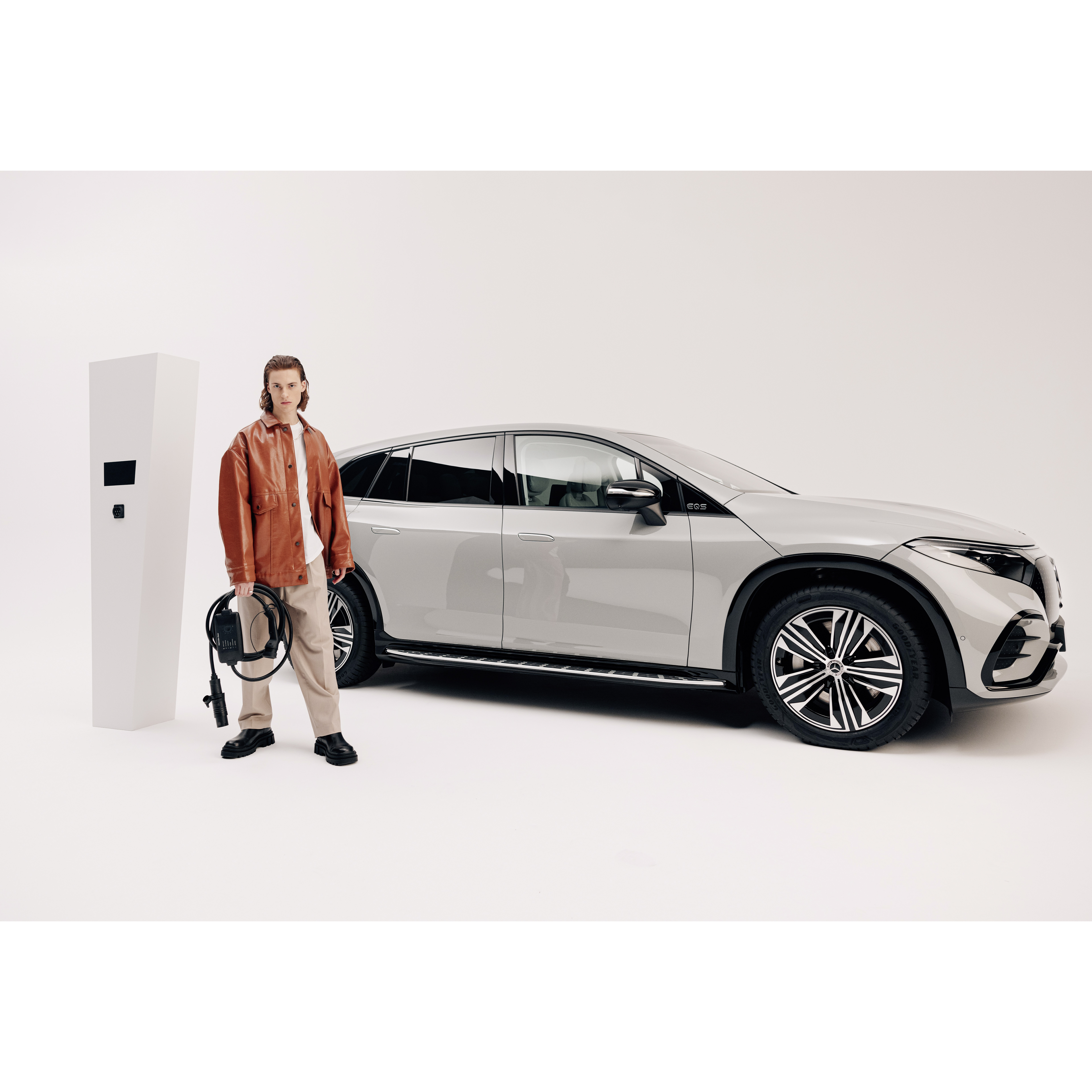 Elastyczny system ładowania Pro | Ładowanie| Mercedes-Benz Mężczyzna obok stacji ładowania i Mercedesa EQS SUV trzymając w ręku przewód do ładowania.