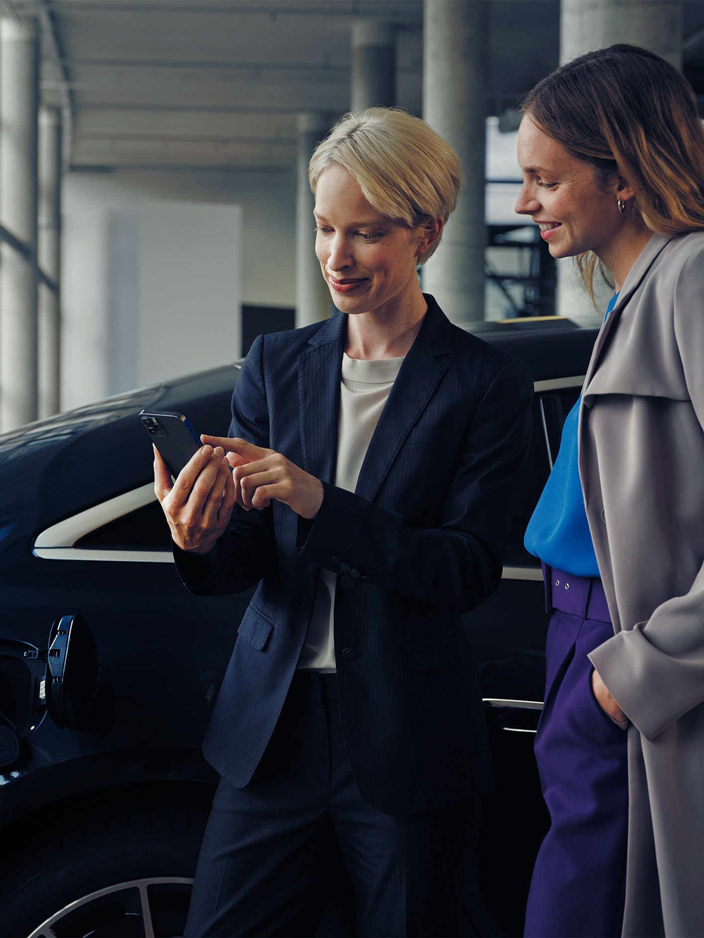 Dwie kobiety w salonie dealerskim patrzą na smartfona.