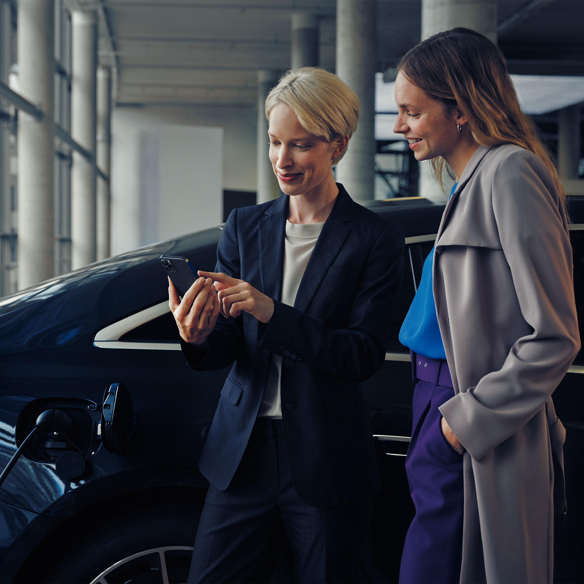 Doradztwo dotyczące instalacji | Ładowanie | Mercedes-Benz Dwie kobiety w salonie dealerskim patrzą na smartfona.