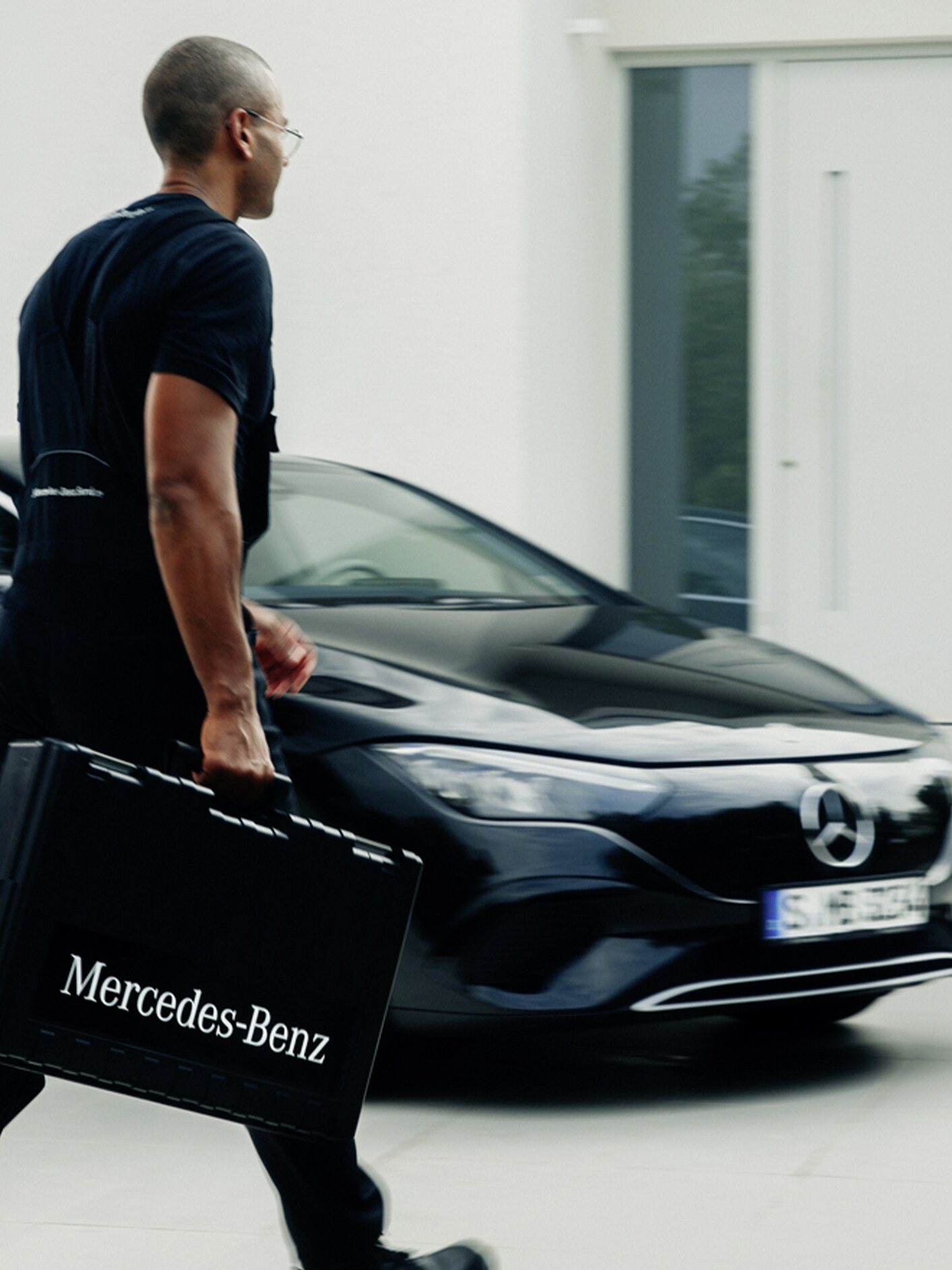 Technik Mercedes-Benz z walizką na narzędzia przechodzi obok czarnego Mercedesa EQE.