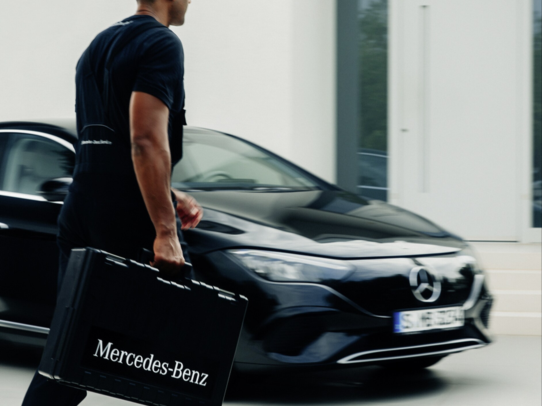 Technik Mercedes-Benz z walizką na narzędzia przechodzi obok czarnego Mercedesa EQE.