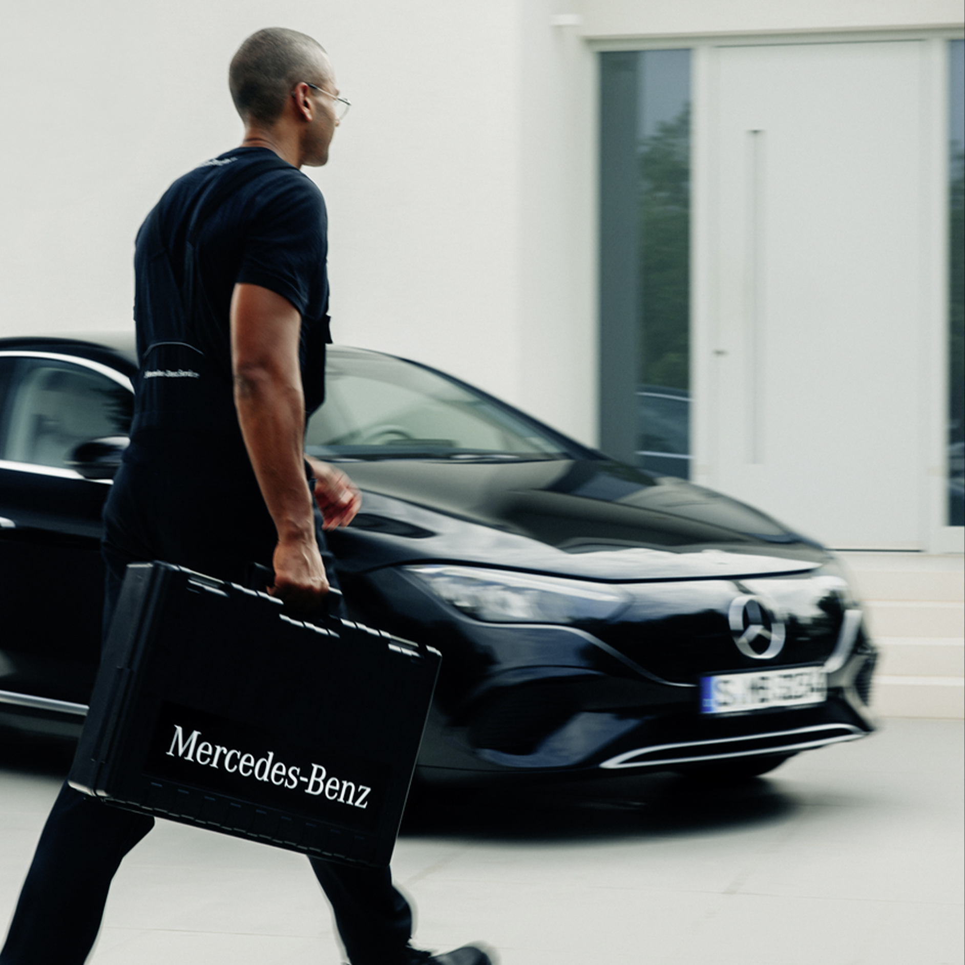 Instalacja | Ładowanie | Mercedes-Benz Technik Mercedes-Benz z walizką na narzędzia przechodzi obok czarnego Mercedesa EQE.