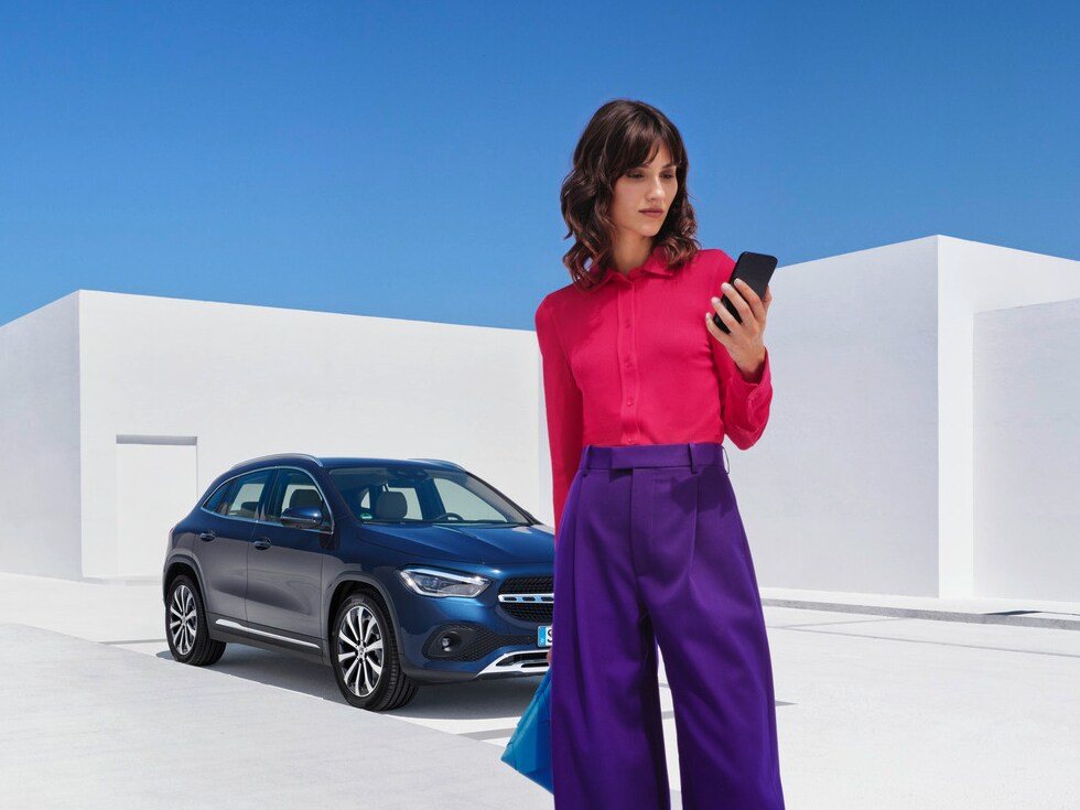 Kobieta z telefonem przed pojazdem Mercedes-Benz.