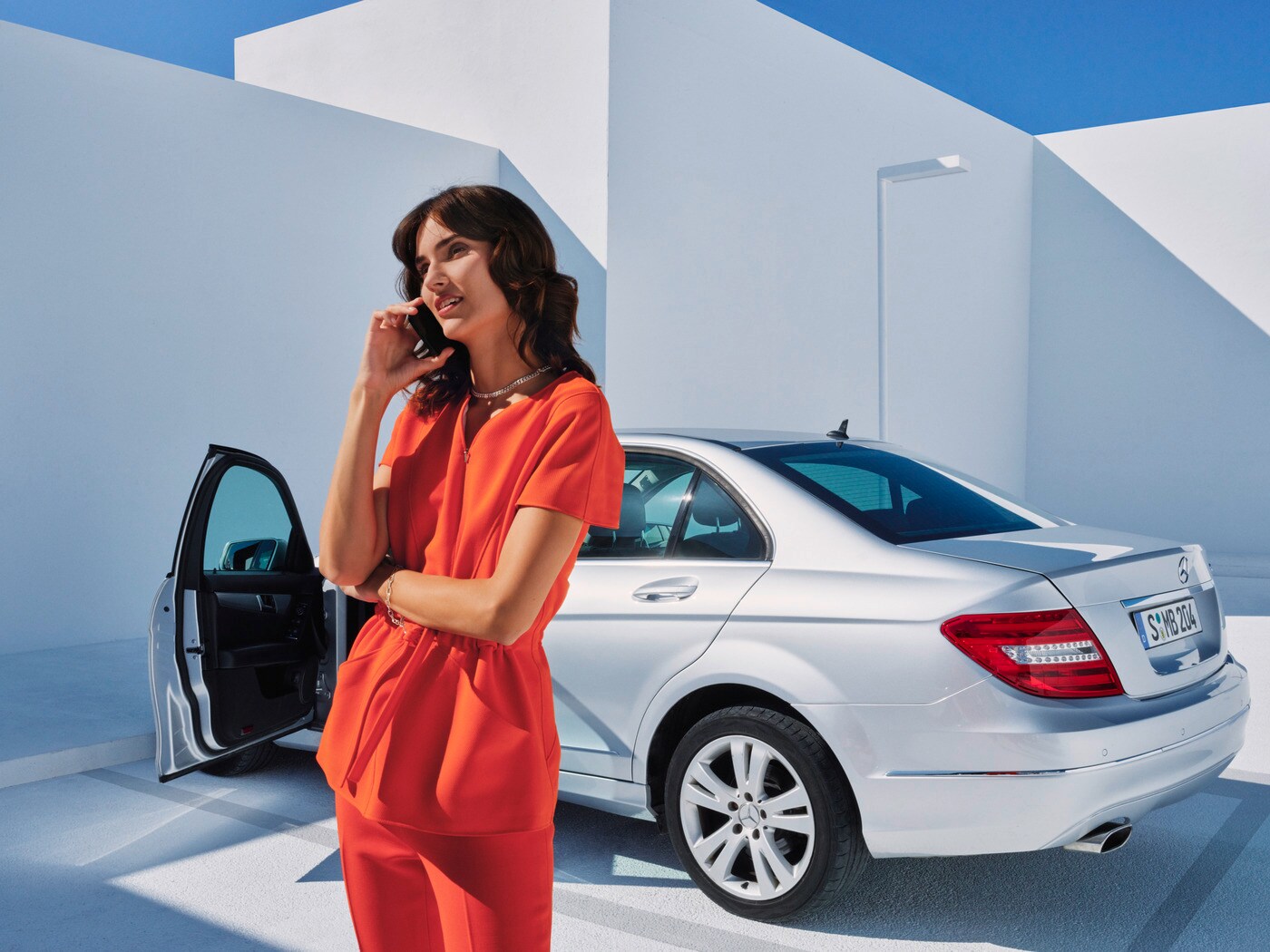 Kobieta prowadząca rozmowę telefoniczną przed pojazdem Mercedes-Benz.
