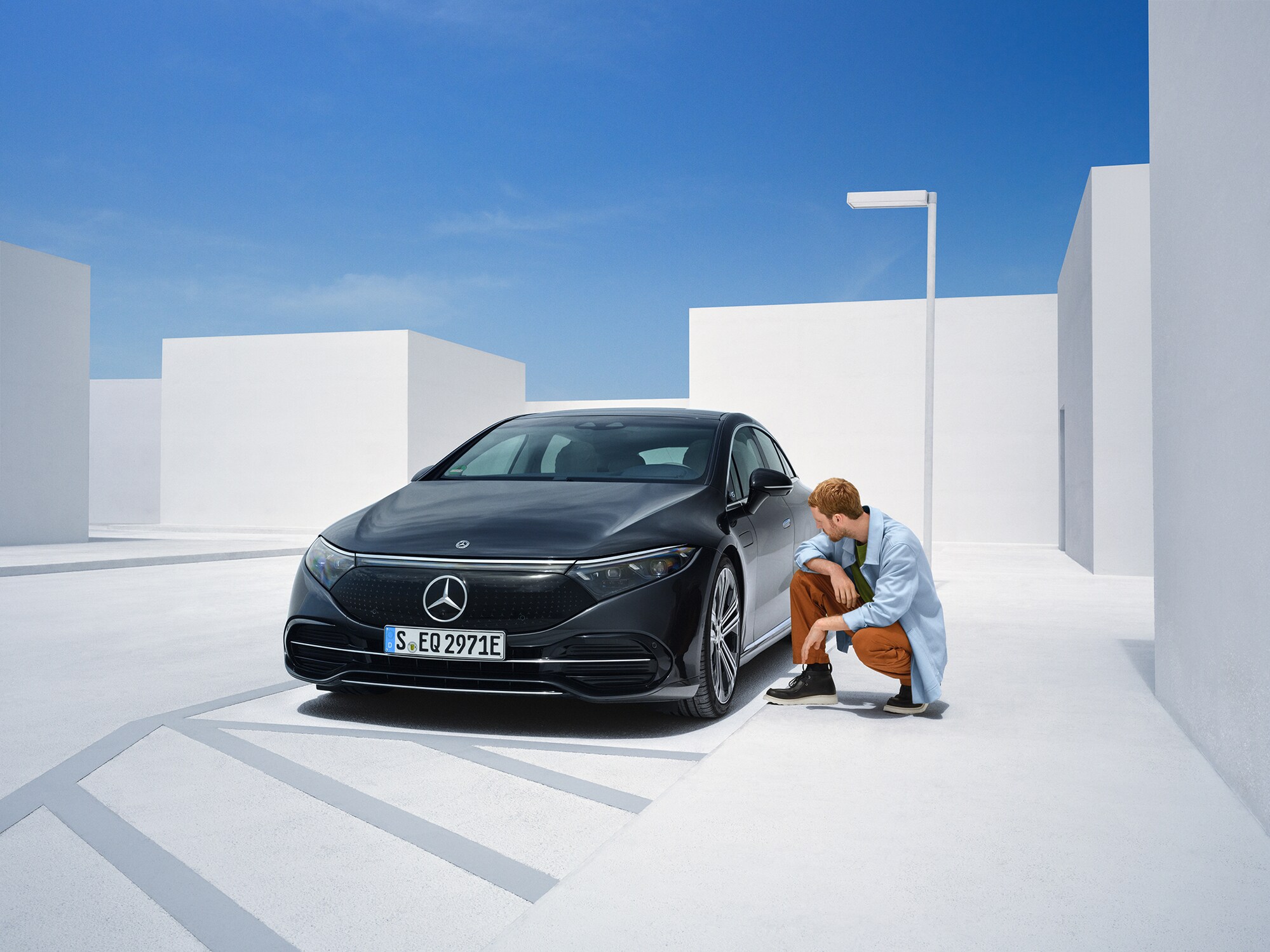 Mężczyzna klęczy przy jednym z boków samochodu Mercedes-Benz i sprawdza jego stan