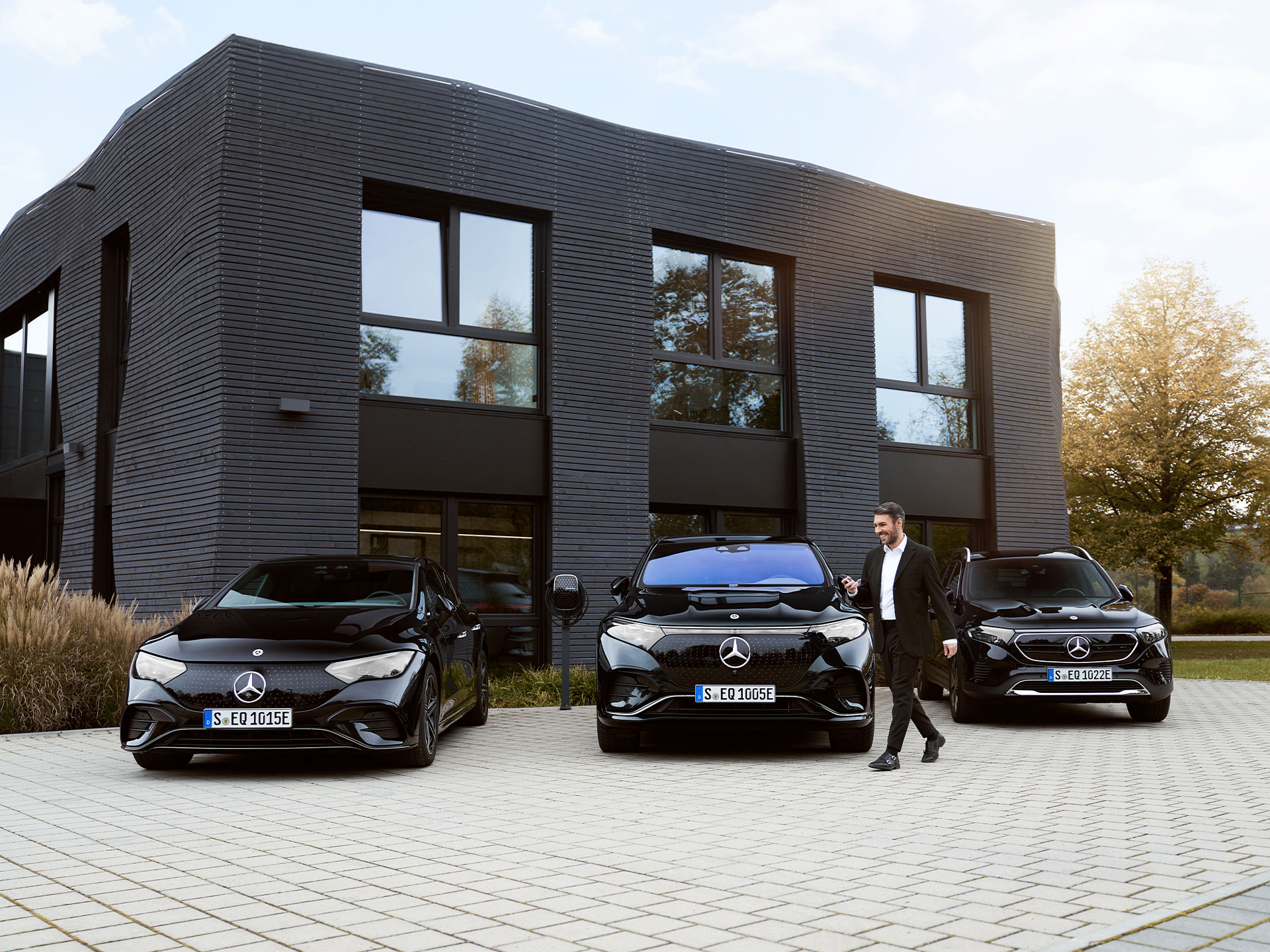 Ładowanie w bazie pojazdów flotowych | Ładowanie | Mercedes-Benz Trzy samochody elektryczne Mercedes-Benz przed budynkiem biurowym.