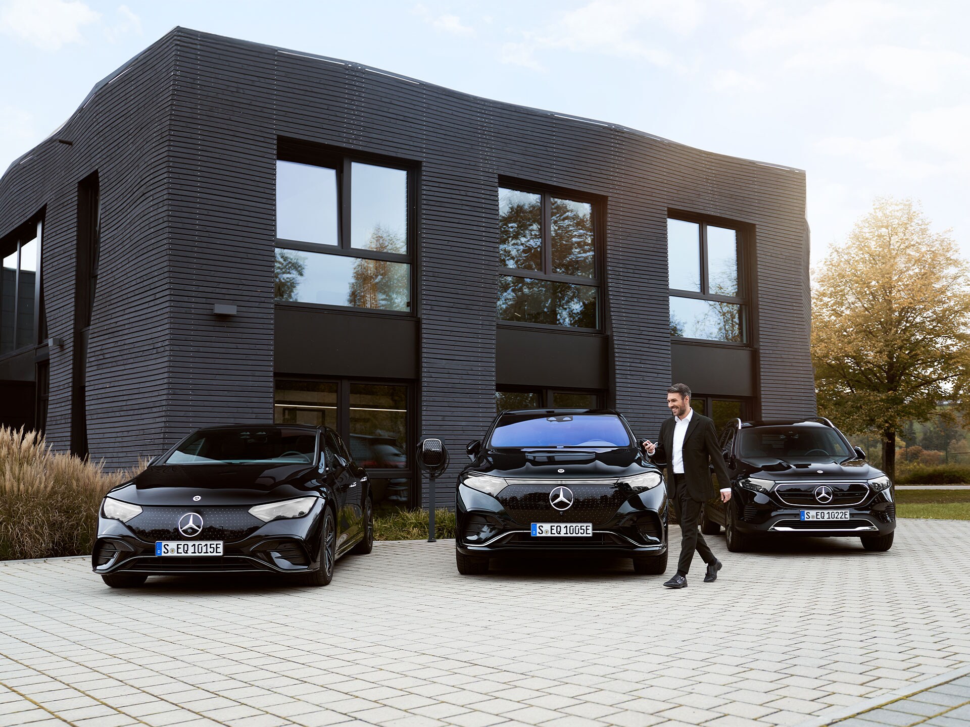Trzy samochody elektryczne Mercedes-Benz przed budynkiem biurowym.