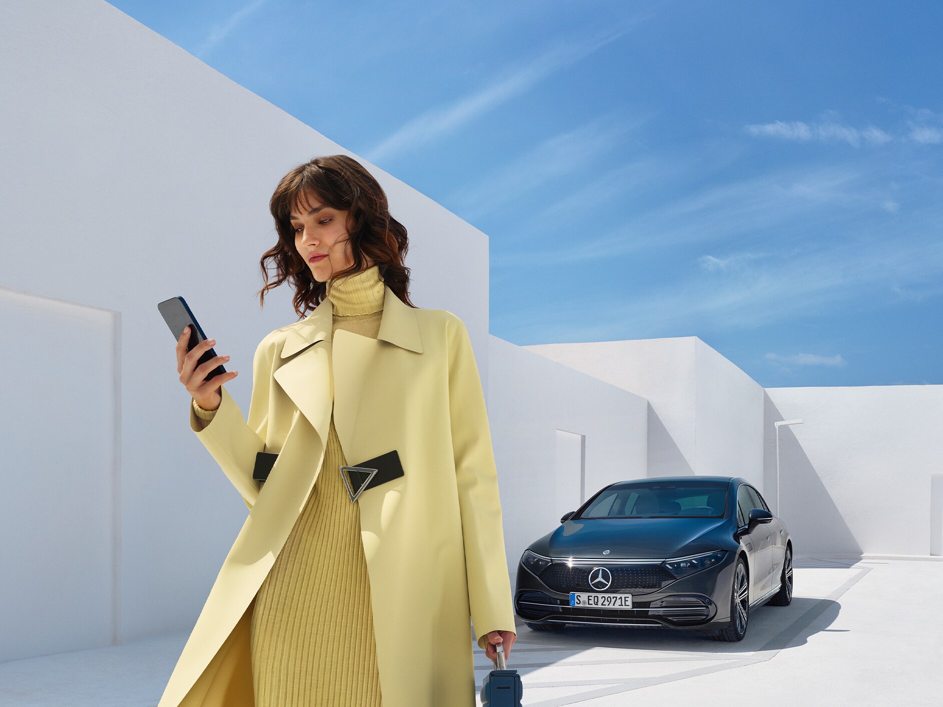 Kobieta patrzy na swój telefon komórkowy, odchodząc od swojego pojazdu Mercedes-Benz z technologią EQ.