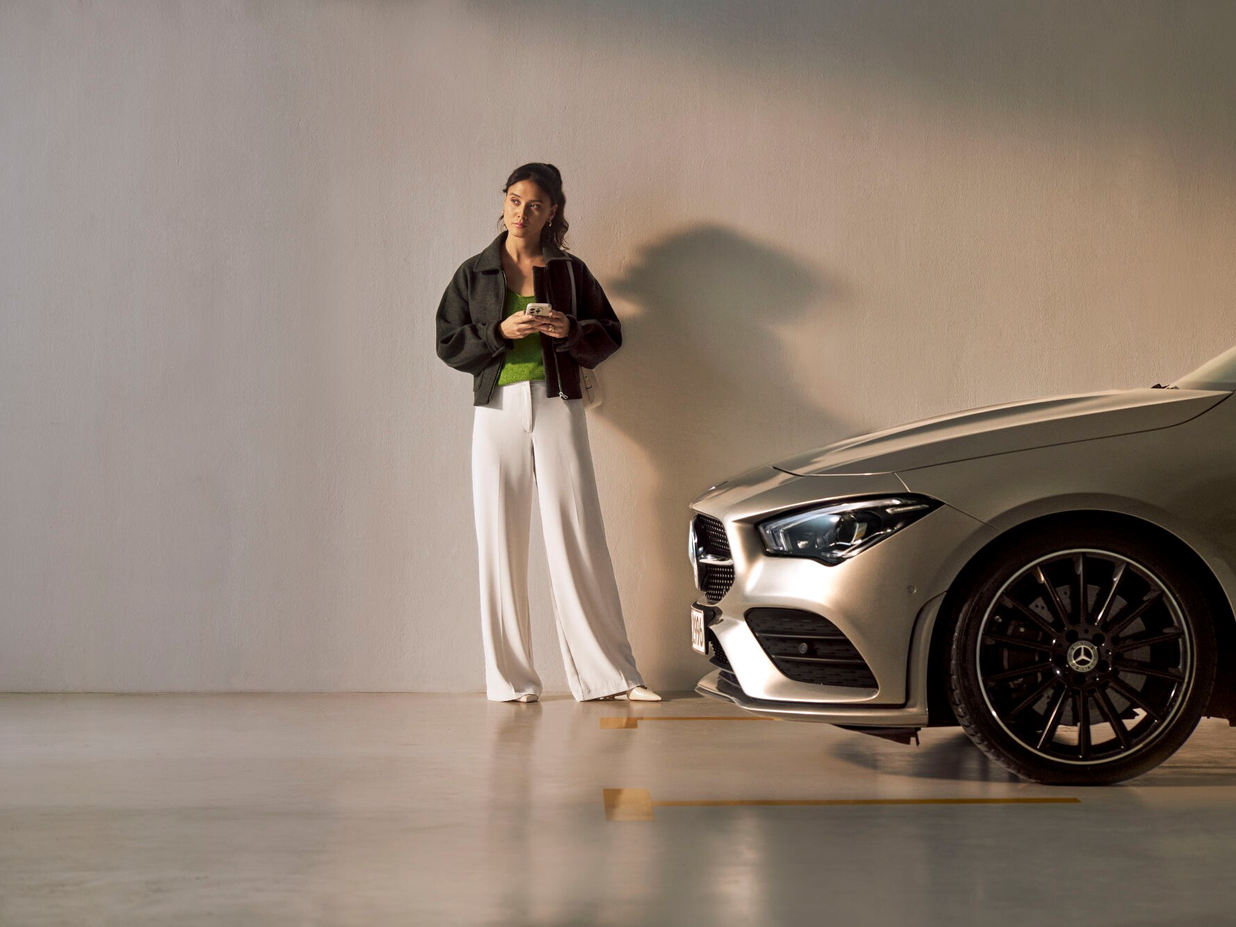 Kobieta ze smartfonem w ręce stojąca bokiem do samochodu Mercedes-Benz.