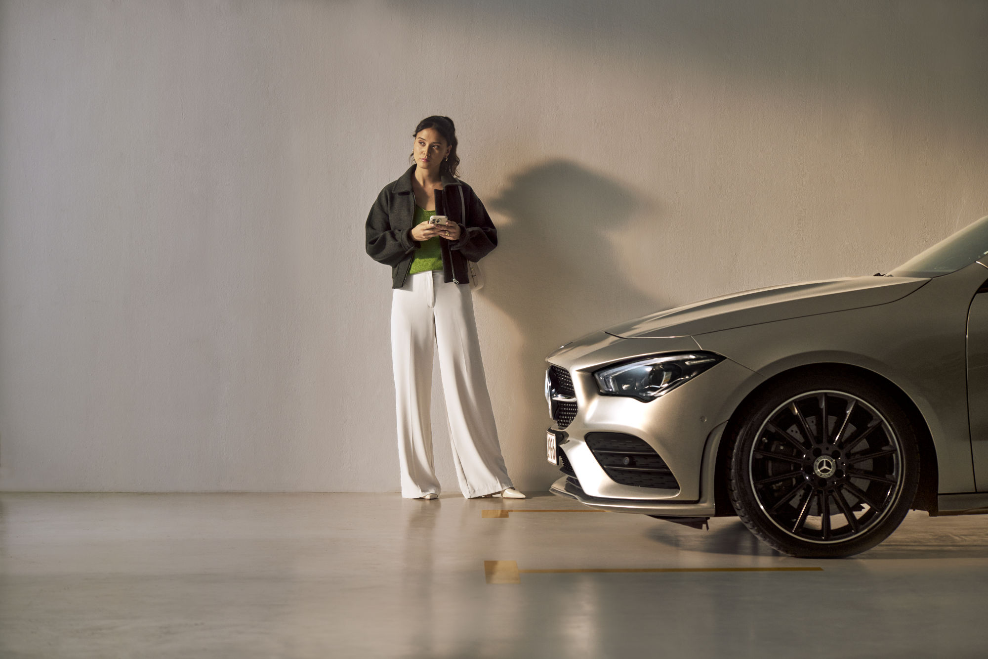 Twój Mercedes wraca do domu! Kobieta ze smartfonem w ręce stojąca bokiem do samochodu Mercedes-Benz.