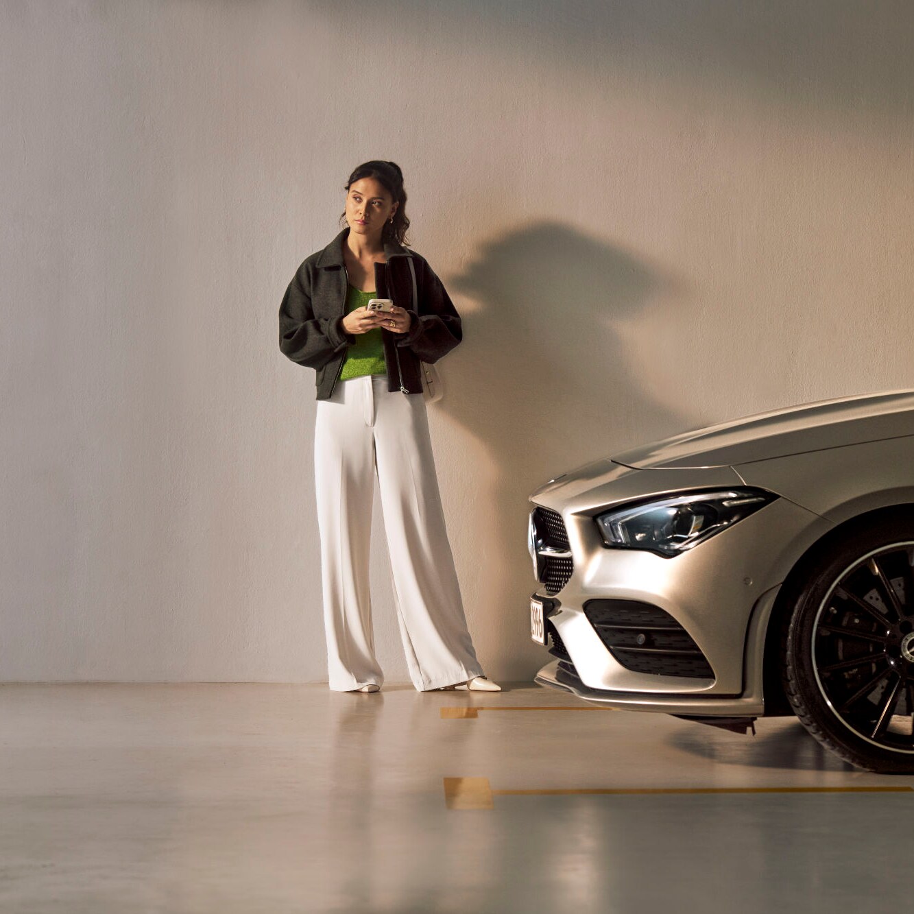 Kobieta stoi przed pojazdem Mercedes-Benz i patrzy na swojego smartfona