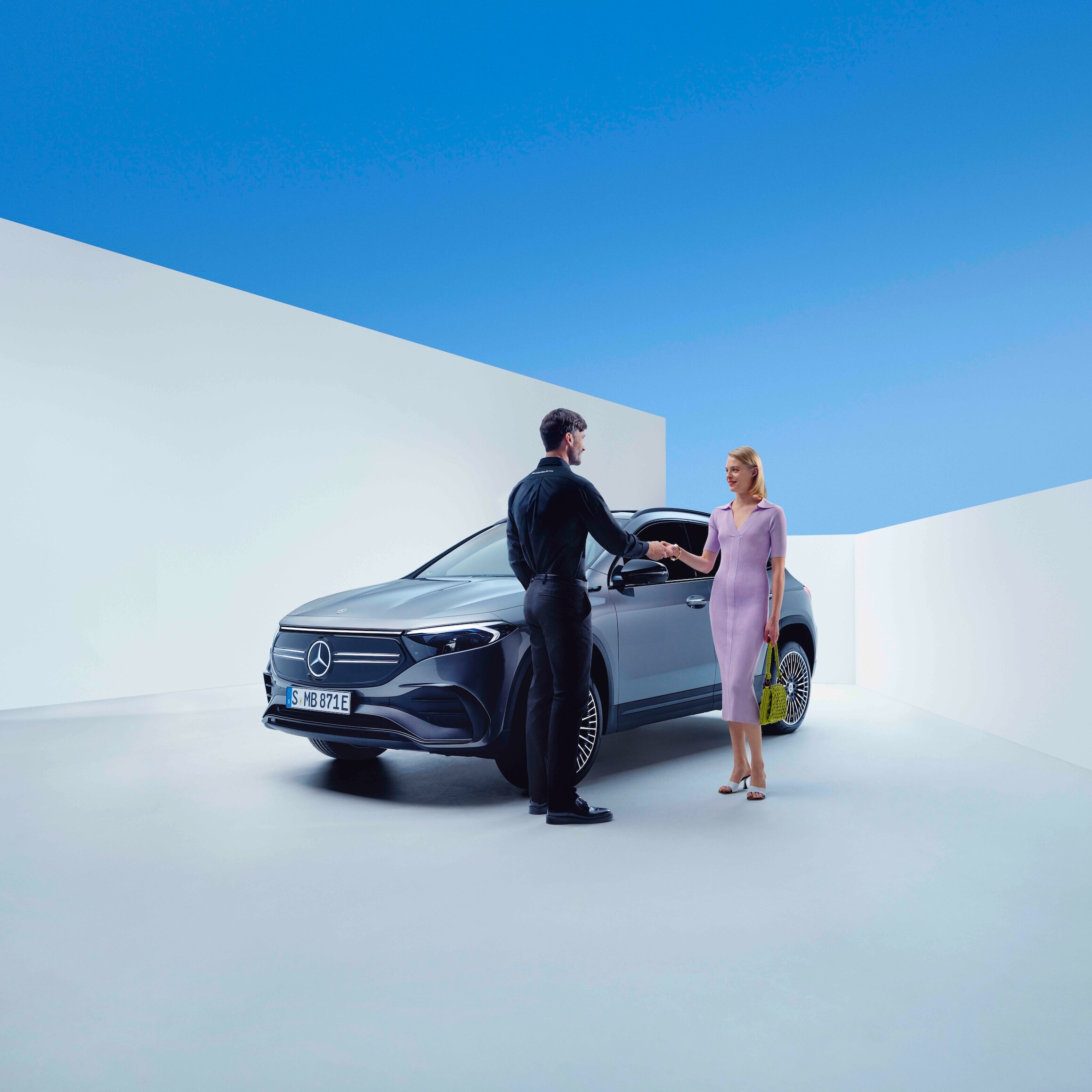 Pracownik Mercedes-Benz i&nbsp;kobieta wymieniają uścisk dłoni przed Mercedesem EQA.