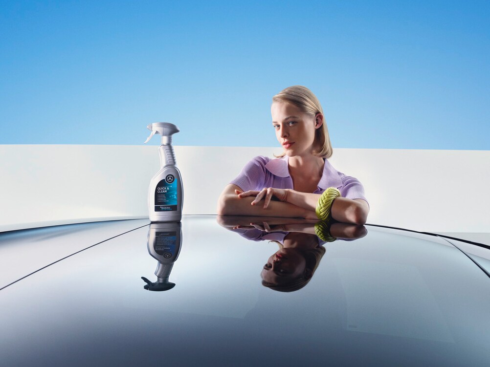 Kobieta opierająca się o samochód Mercedes-Benz z produktami do czyszczenia i regeneracji.