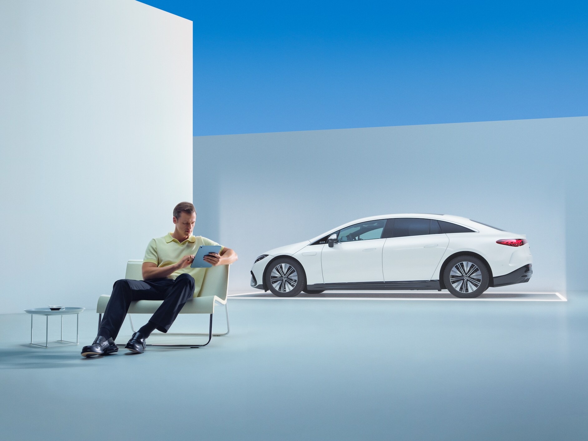 Osoba siedzi przed swoim Mercedesem i korzysta z tabletu.