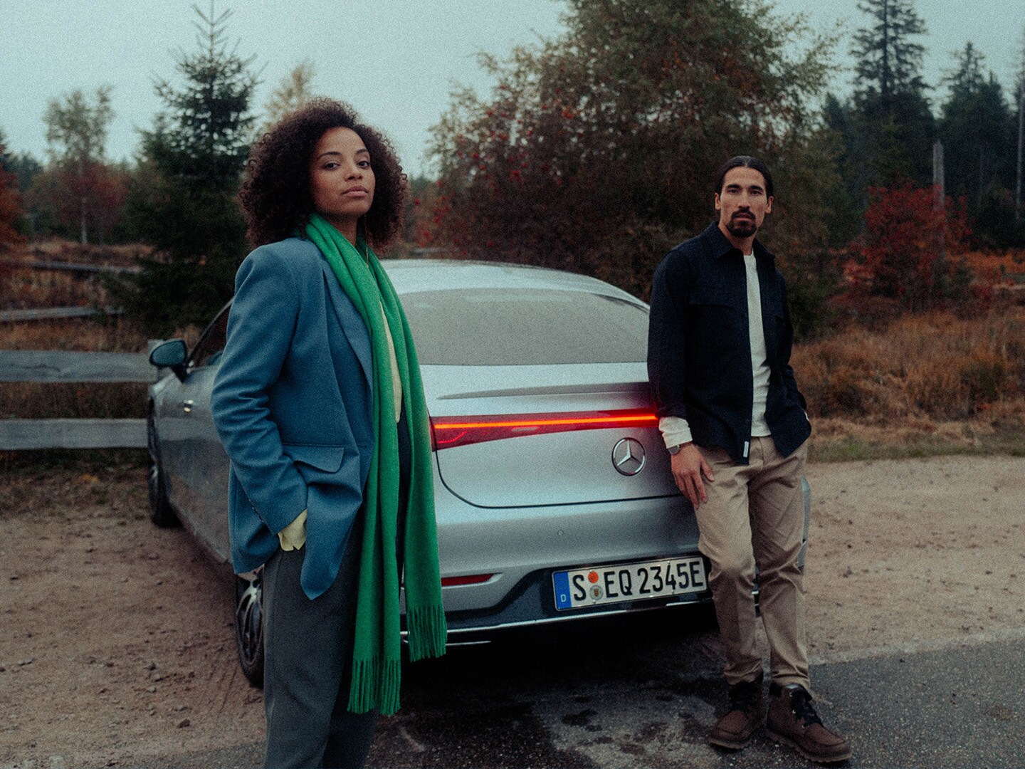 Kobieta i mężczyzna stoją z tyłu zaparkowanego na żwirowym parkingu EQS limuzyna.