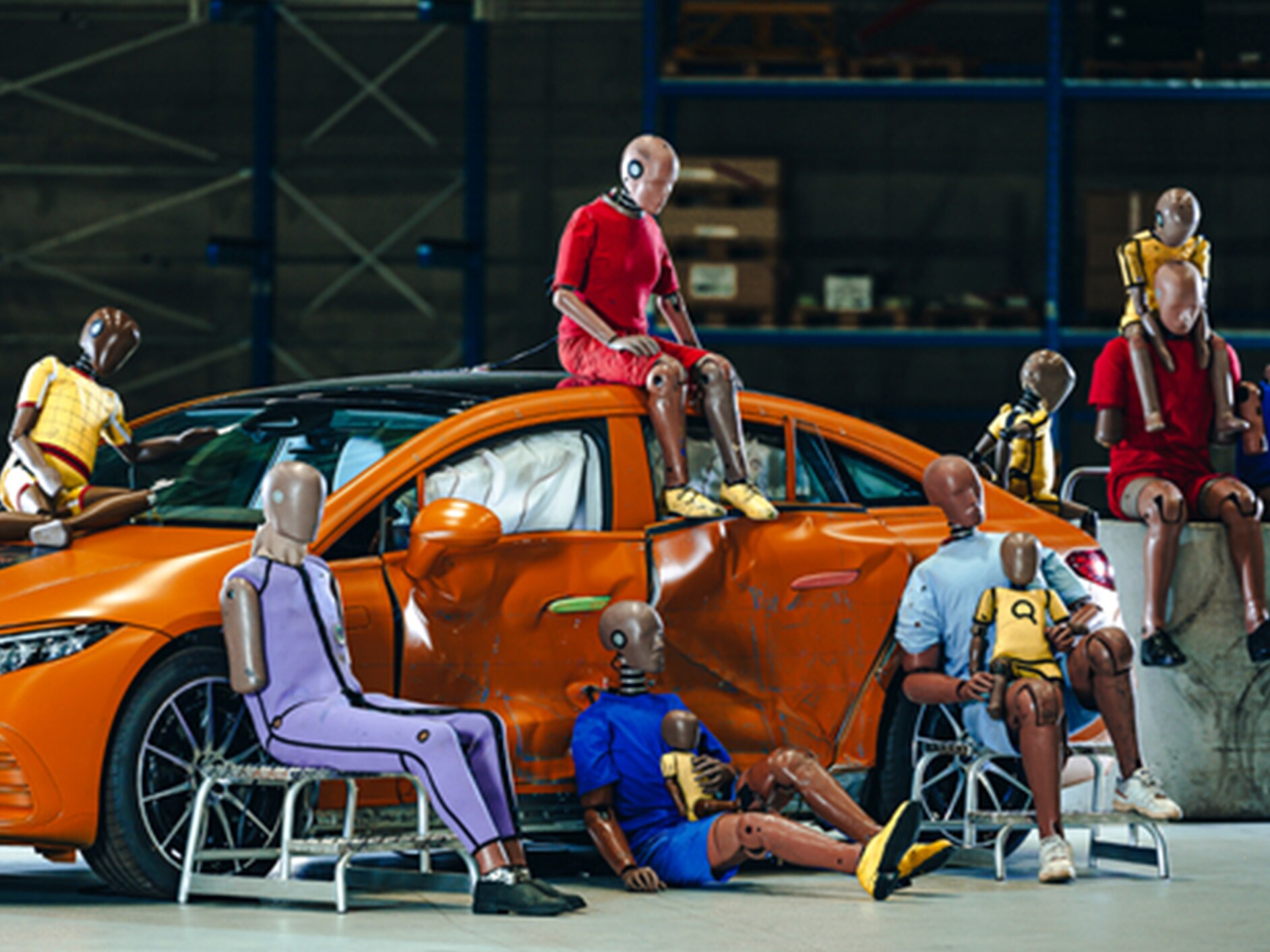Wiele manekinów do testów zderzeniowych siedzących na i wokół samochodu Mercedes-Benz.