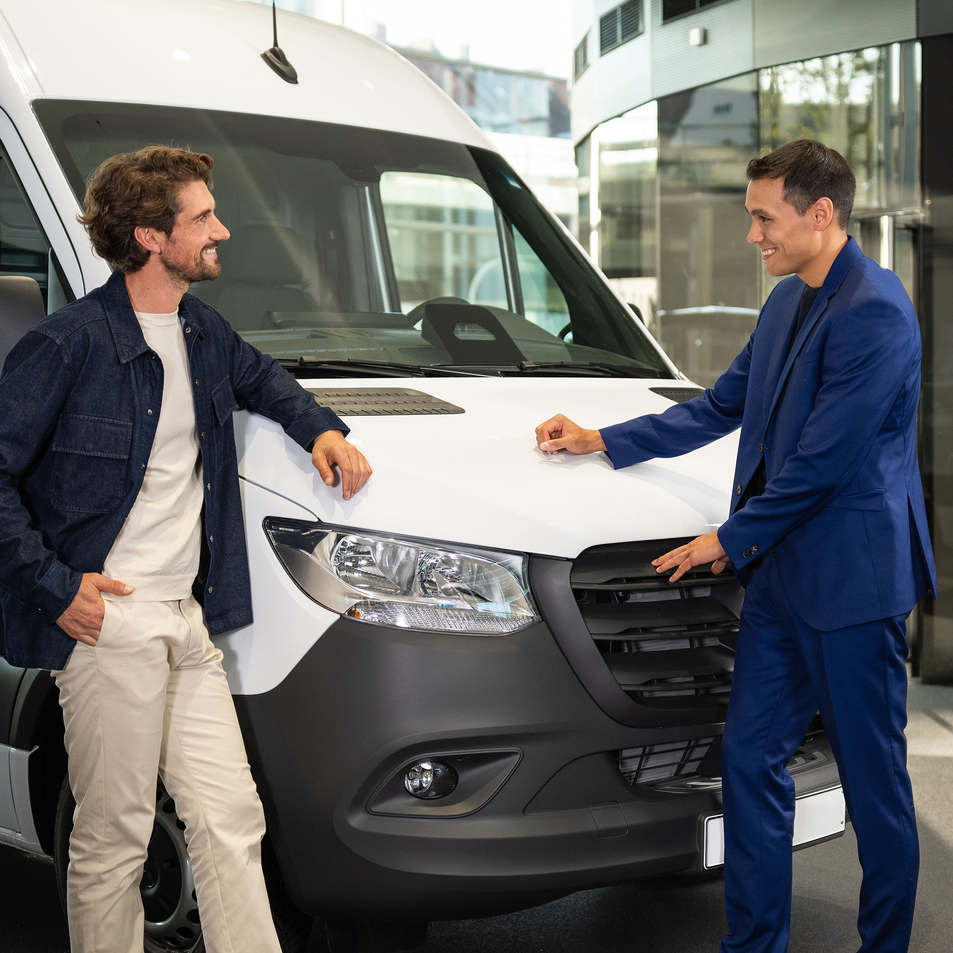 Ubezpieczenie Twojego samochodu Mercedes-Benz Dwie osoby opierające się o samochód dostawczy Mercedes-Benz i prowadzące rozmowę.