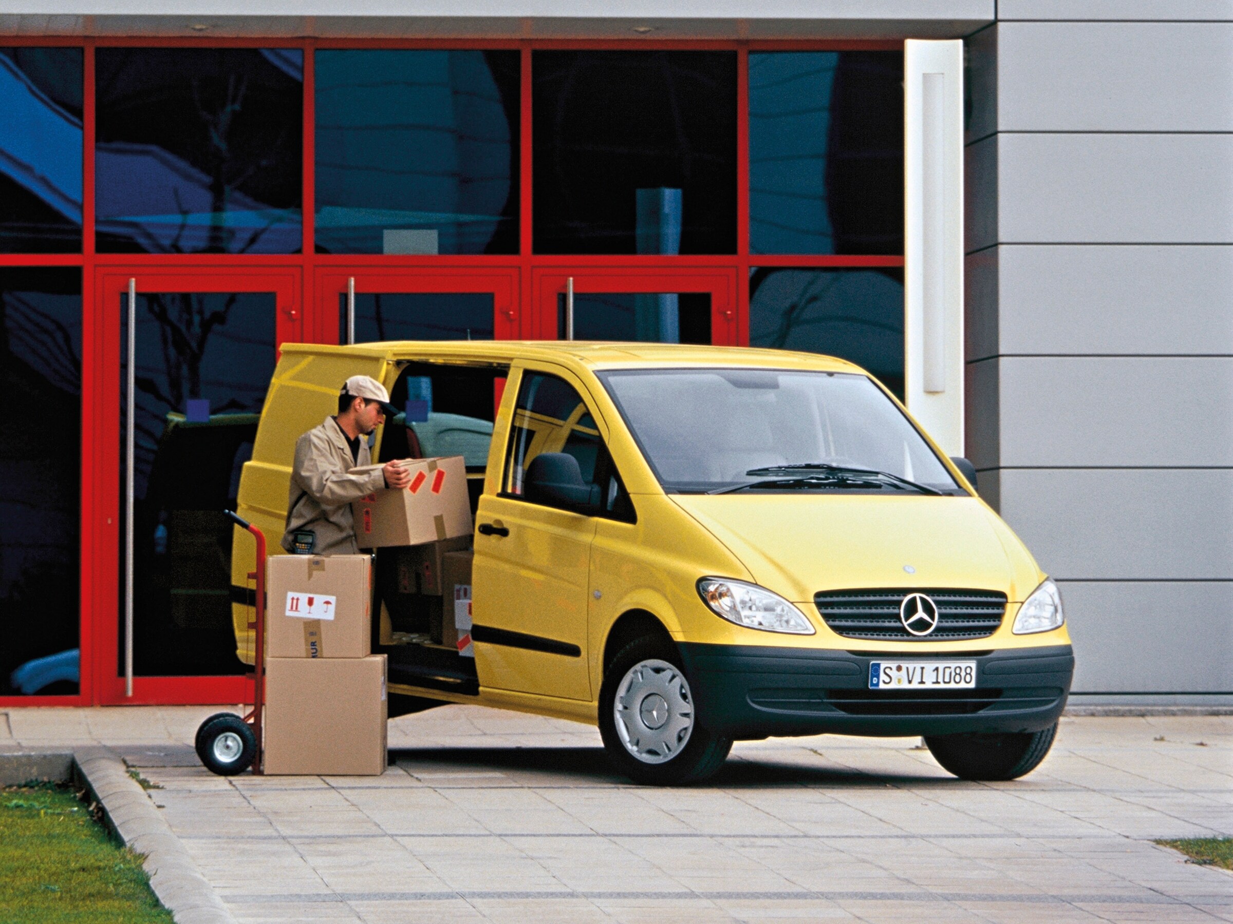 Żółty Mercedes-Benz Vito zaparkowany przed budynkiem i pracownik rozładowujący paczki