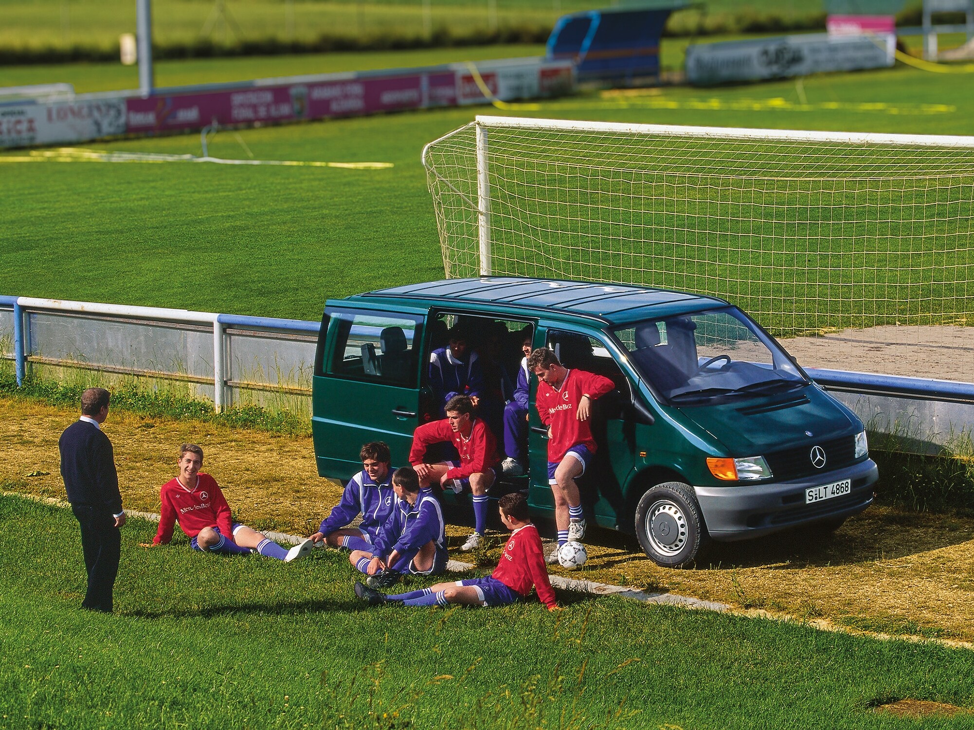 Mercedes-Benz Vito pierwszej generacji zaparkowany obok boiska piłkarskiego, a w pobliżu gracze drużyny