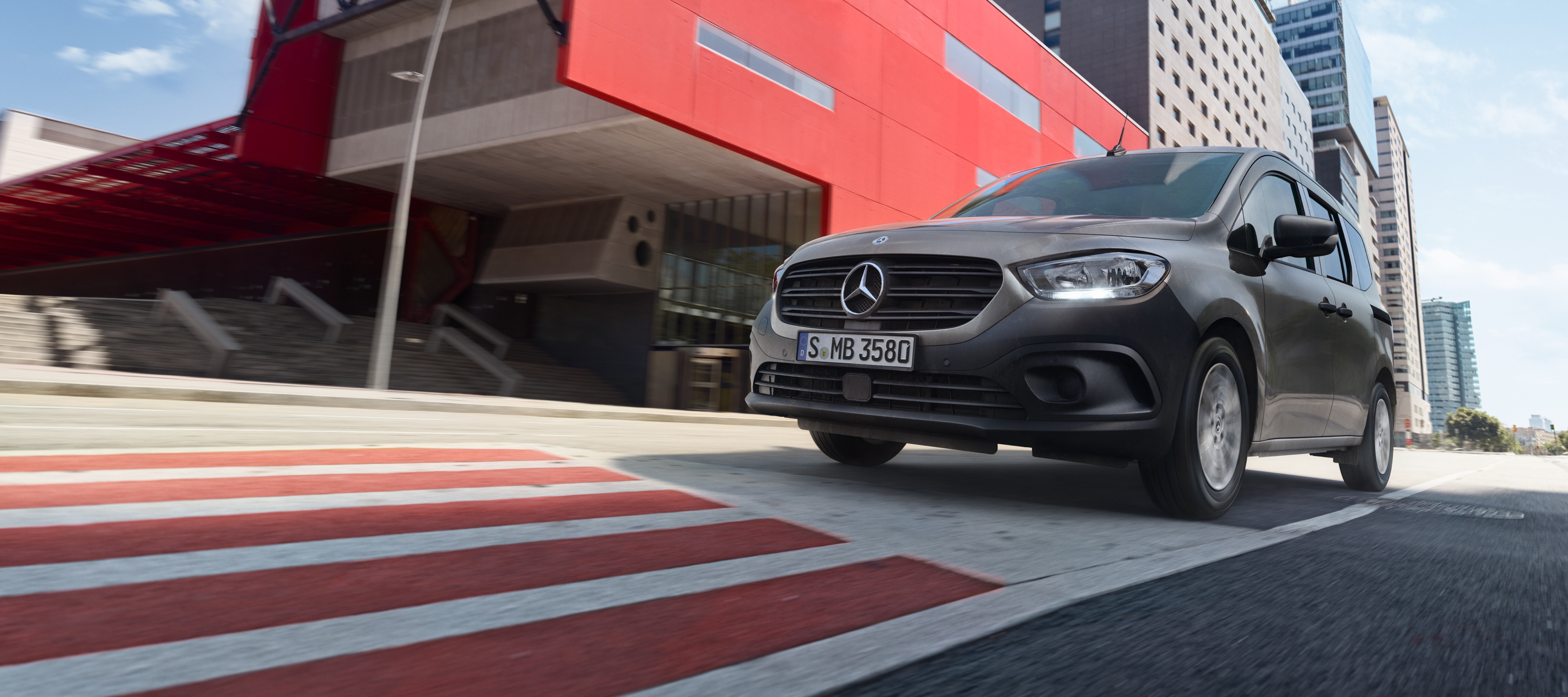 Citan Tourer | Samochody dostawcze Mercedes-Benz Citan Tourer, kompaktowy samochód dostawczy od Mercedes-Benz, jedzie przez nowoczesną aglomerację miejską.