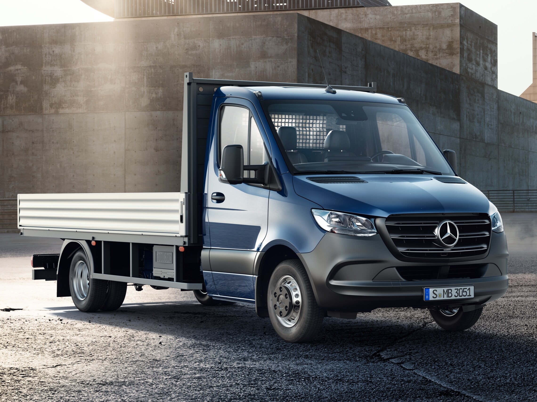 Granatowy Sprinter Podwozie ze skrzynią ładunkową na tle budynków przemysłowych.