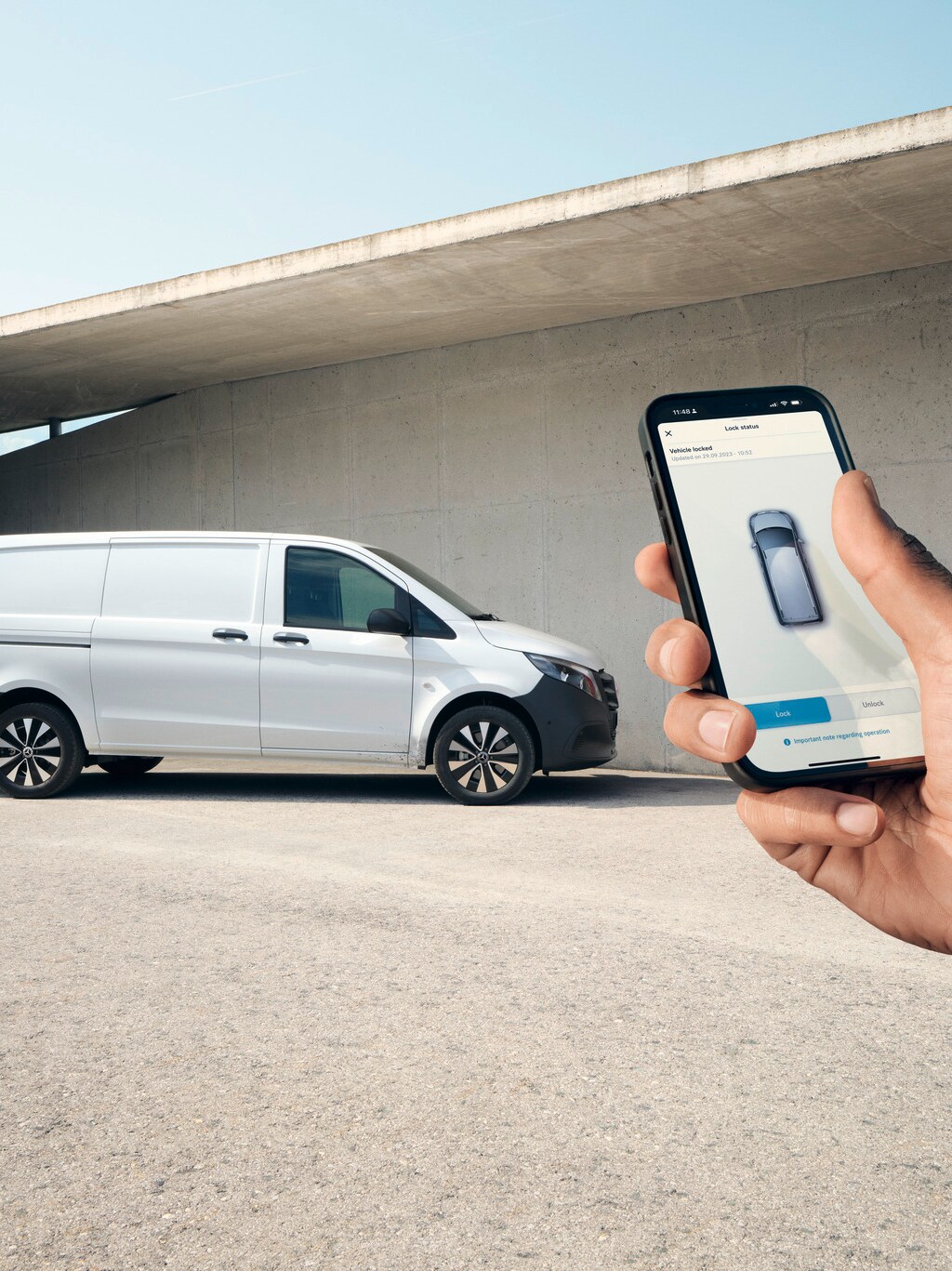 Dłoń trzymająca smartfona wyświetlającego aplikację Mercedes-Benz. Vito Furgon widoczny w tle.