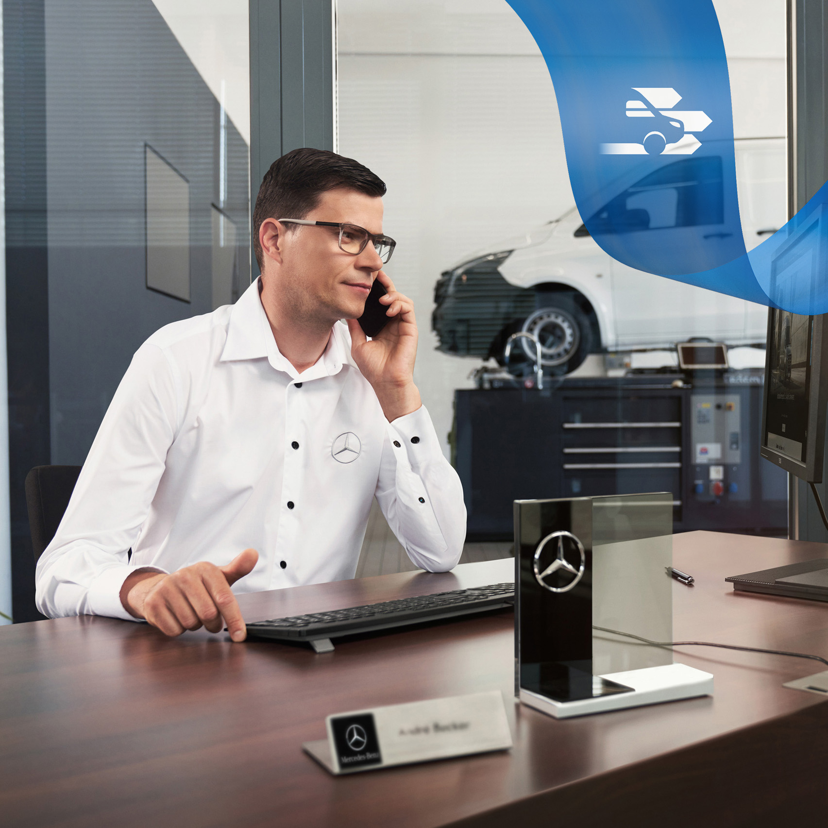 Eksperci pomocy drogowej Mercedes-Benz Pracownik przy biurku rozmawiający przez telefon i samochód dostawczy Mercedes-Benz Vito w warsztacie w tle.