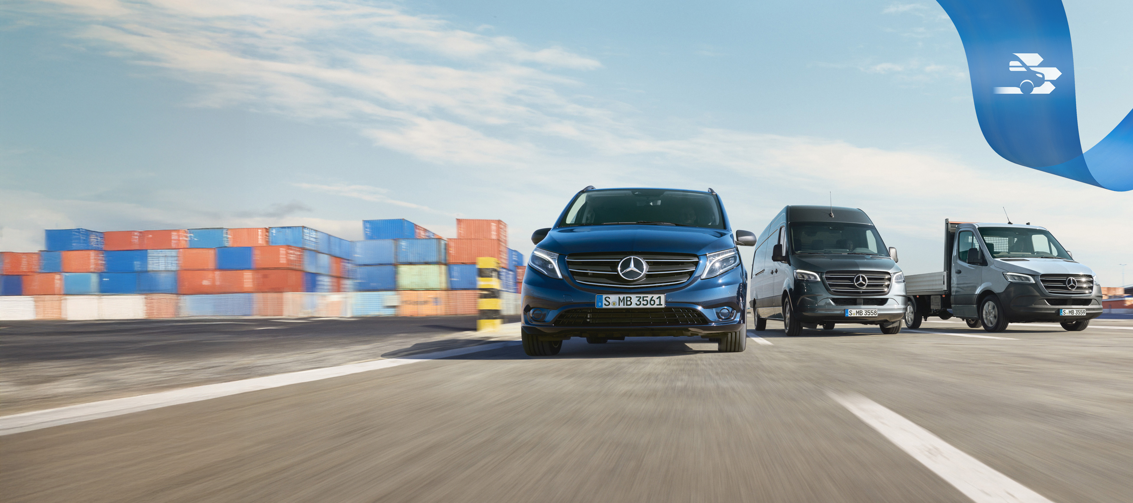 Mobilovan | Samochody dostawcze Mercedes-Benz Grupa samochodów dostawczych Mercedes-Benz na drodze z kontenerami dostawczymi w tle.