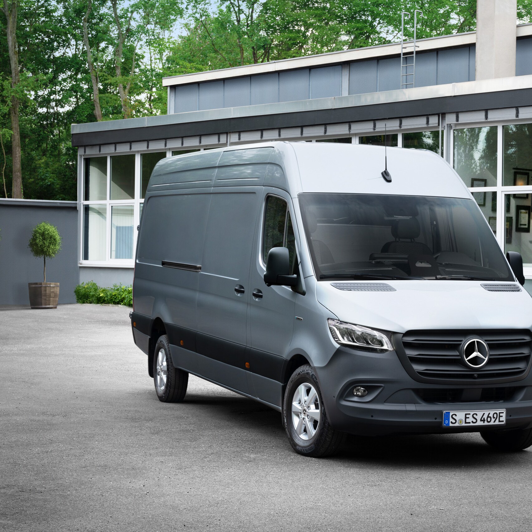 Szary samochód Mercedes-Benz Sprinter stojący przed biurem z osobą trzymającą smartfon na pierwszym planie.